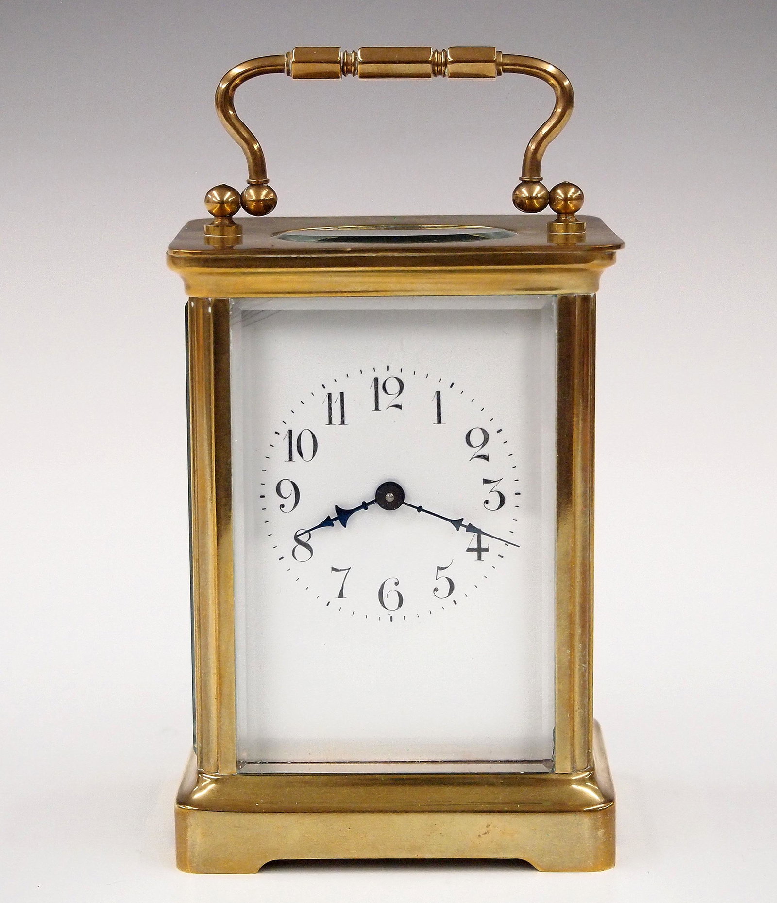 French Carriage Clock: Early 20th century H & H French carriage clock. 8-day time only movement with porcelain dial and Arabic numerals. Brass case with swing handle and beveled glasses on a molded base. Some wear, hairline