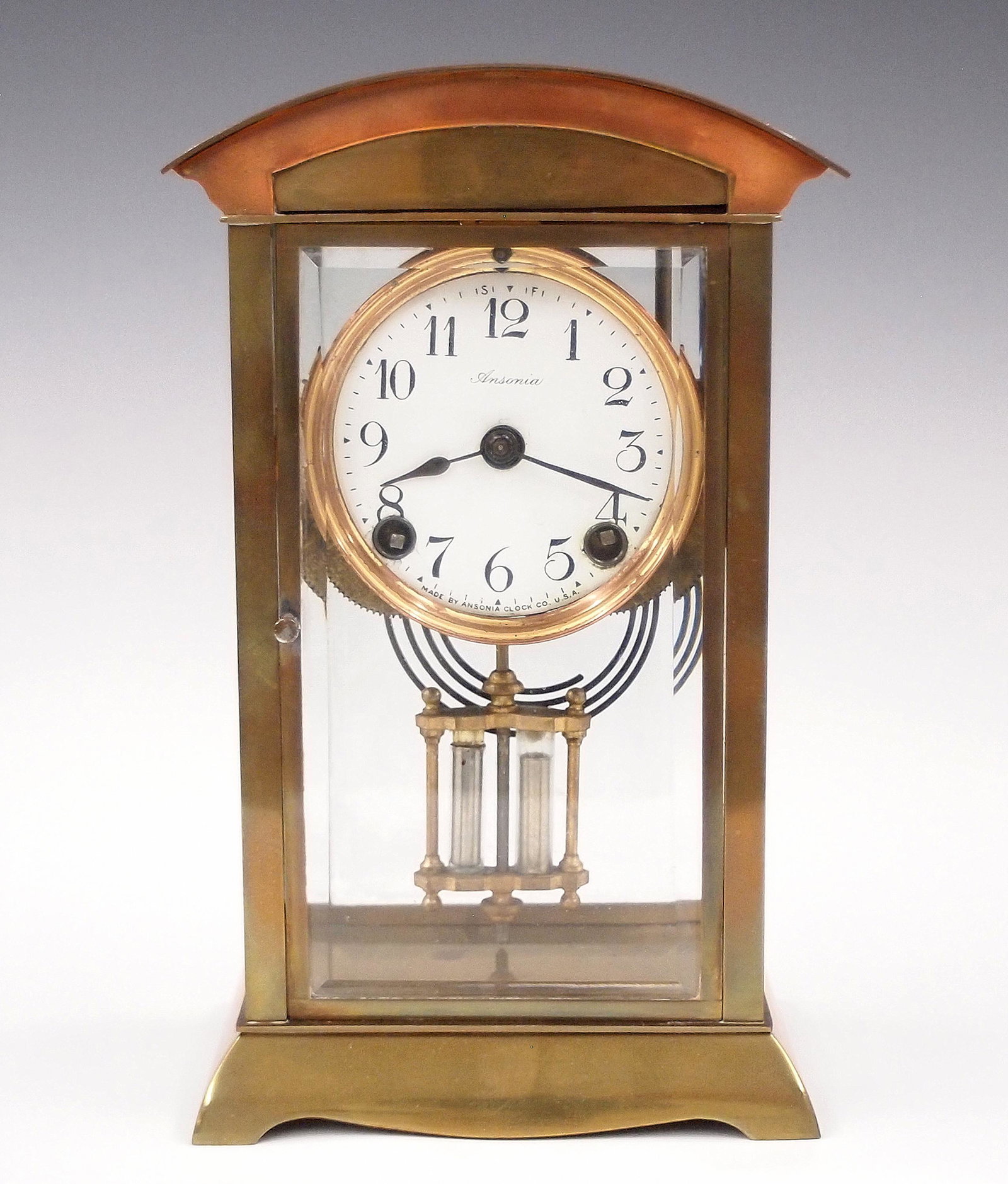 Ansonia Crystal Regulator: A early 20th century Ansonia Crystal Regulator. 8-day time and strike movement with porcelain dial and Arabic numerals. Brass case with double glass panels, arched top and molded base. Wear, minor dam