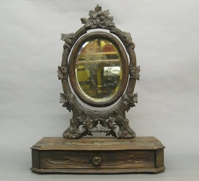 Carved shaving mirror: A late 19th century Black Forest carved Walnut shaving mirror. Extensive hand carved detail with a tilt mirror and lower drawer. Old dark finish with some wear. 20 3/4" high. ESTIMATE $100-200