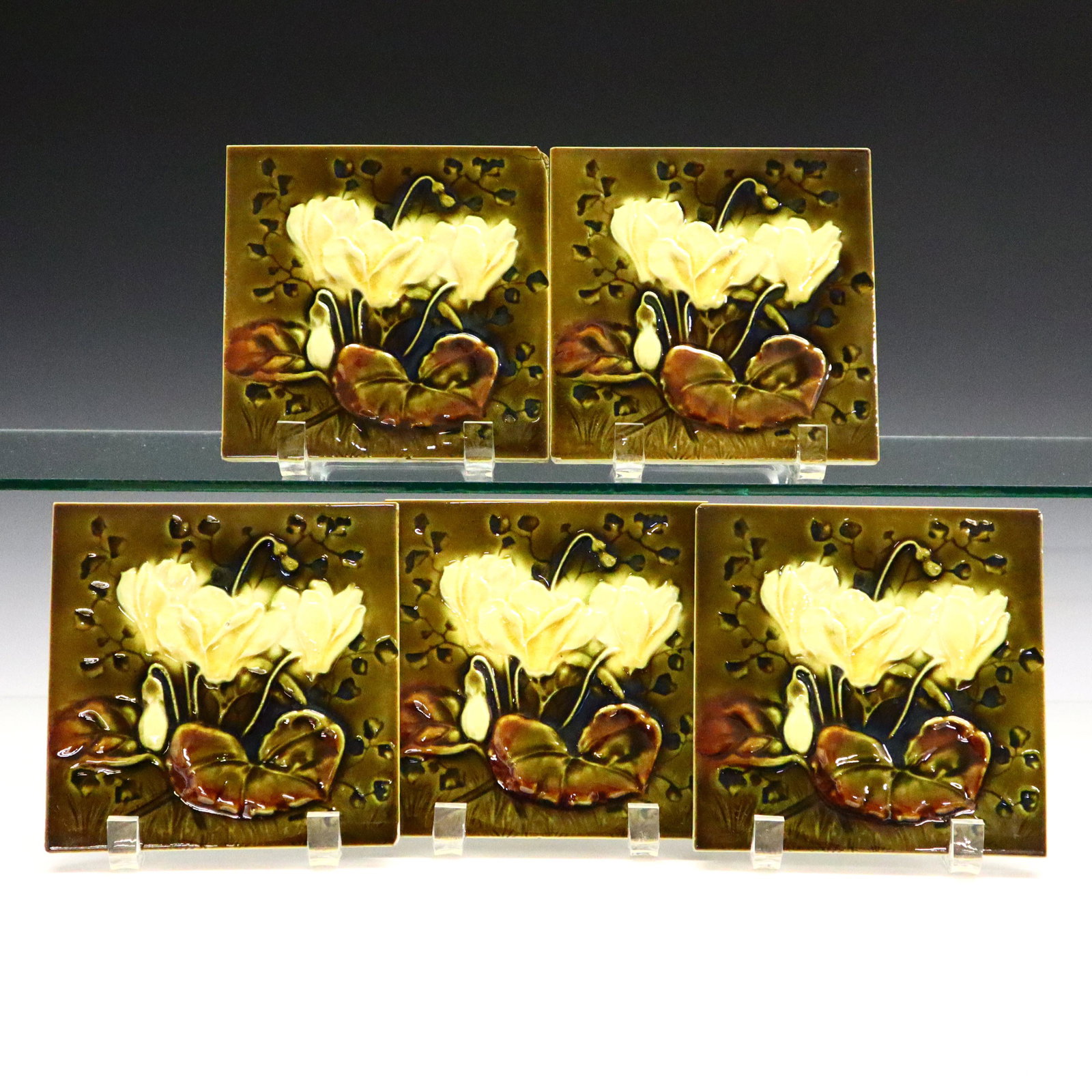 5 J.H. Barrett Tiles: Five Late 19th Century J.H. Barrett earthenware Tiles. Art Nouveau tiles featuring flowers and leaves in colors of olive green, cream, and muted red. Maker's monogram at the underside. Crazing, some f