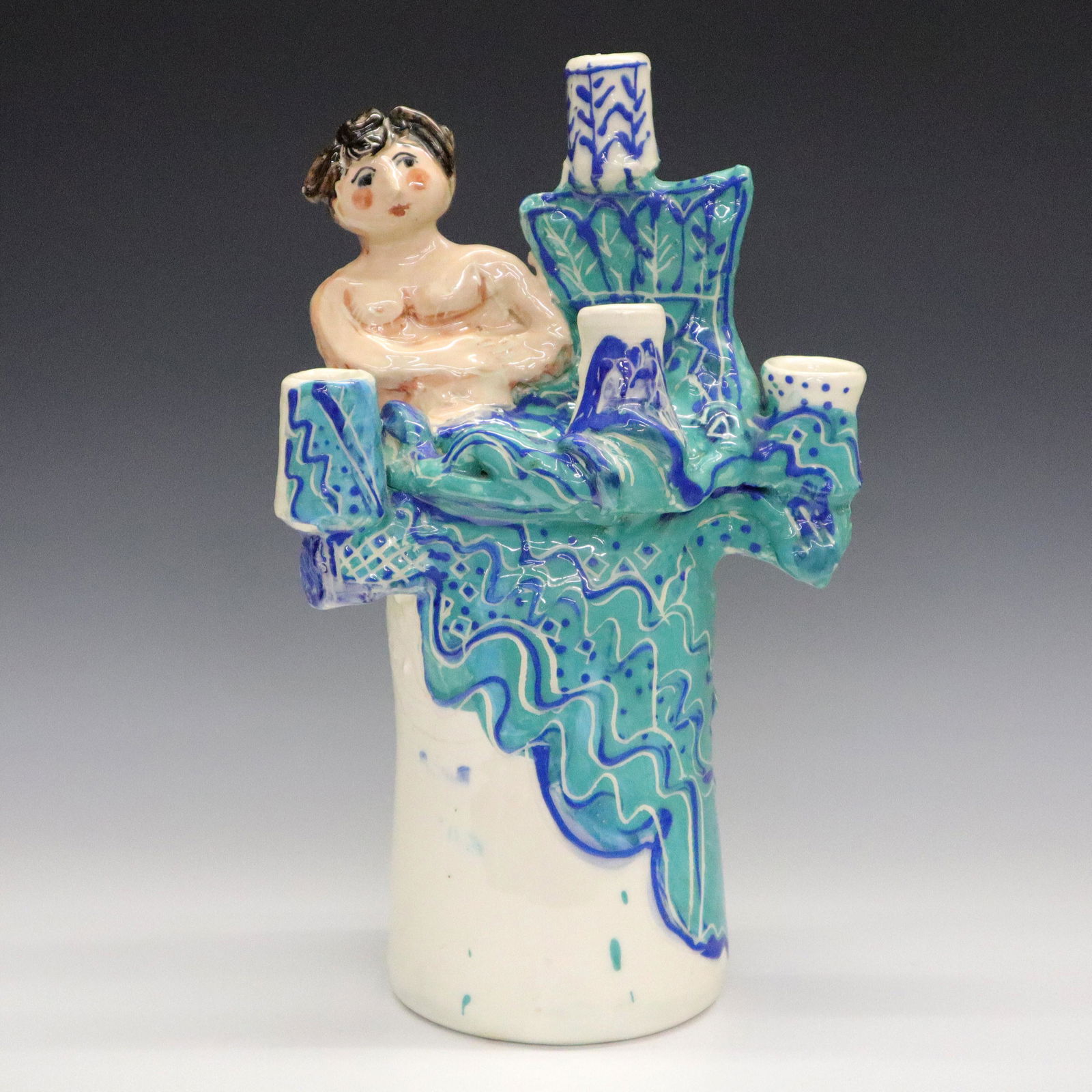 Sue Bolt Candelabra: A late 20th century art pottery candelabra by Sue Bolt. Cylindrical base with five arms, decorated with Blue and Green geometric foliage design and sculpted nude female form. Unsigned. Minor wear. 14