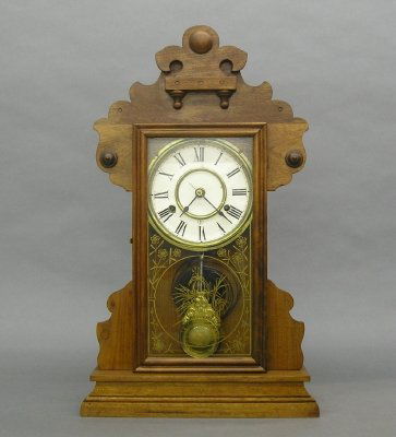 Kitchen Shelf clock: A turn of the century New Haven "Dandy" line Kitchen Shelf clock. 8 day spring driven time and strike movement. Walnut case with applied detail with a single door and decorative glass. Paper label on