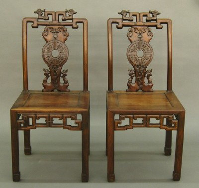 Pr Chinese chairs: A pair of late 19th century Chinese hardwood chairs. Shaped backs with carved design featuring Dragons and Clouds, paneled seats with reticulated skirts and straight legs with scrolled feet. Older fin