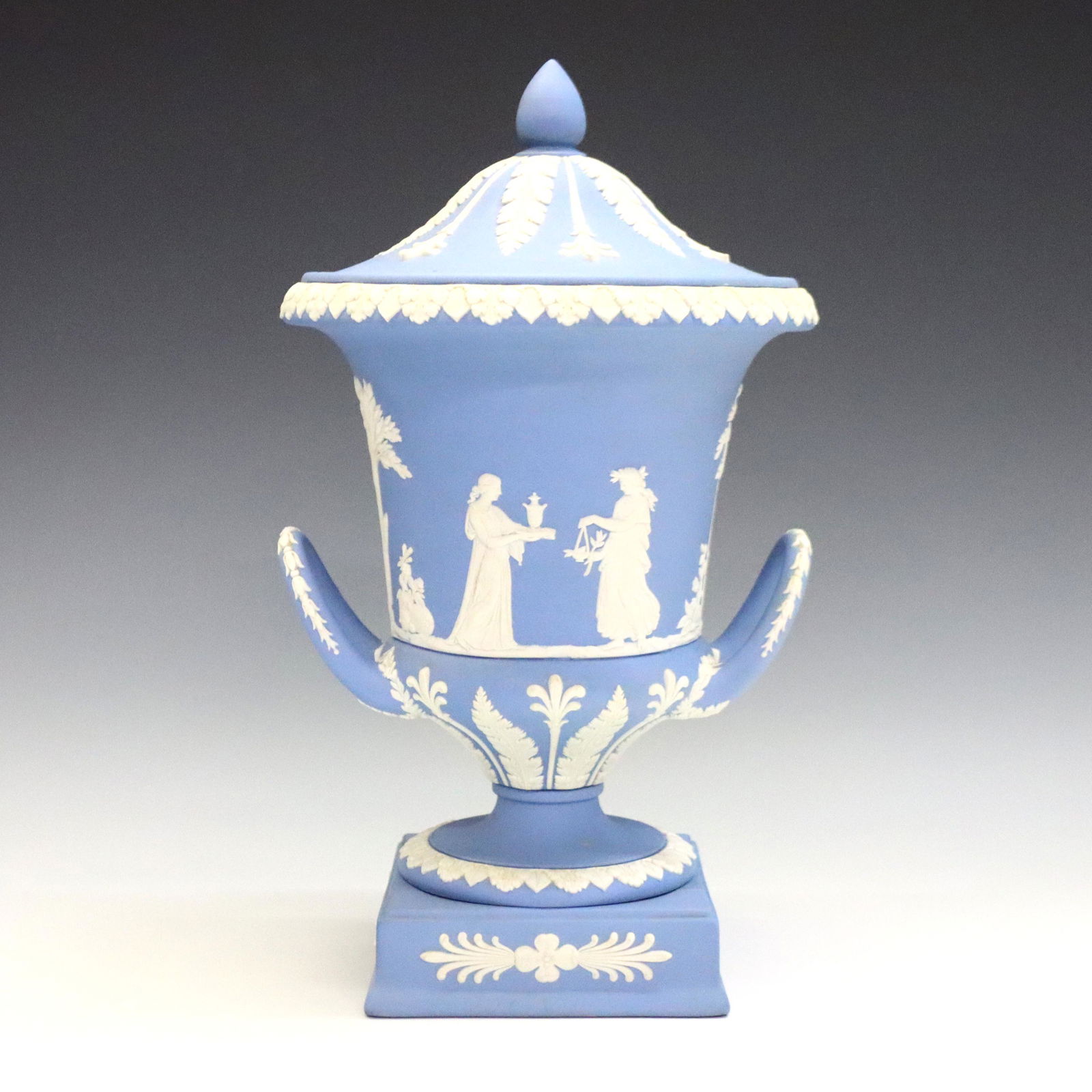 Wedgwood Jasperware Covered Urn: A late 20th century Wedgwood covered urn. Light Blue Jasper dipped body with vintage garlands and classical figures in White relief. Impressed marks. Minor wear. 12" high. ESTIMATE $200-400