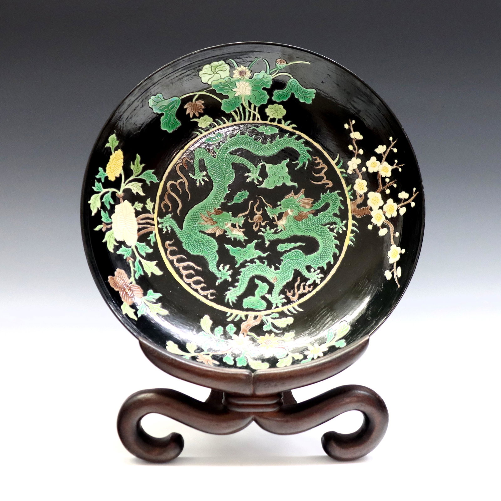 Chinese Famille Noir Bowl: A Chinese Kangxi style Famille Noir porcelain bowl. Hand-painted and incised decoration depicting two dragons chasing a flaming pearl with floral border, on a scrolled Rosewood stand. Painted marks. S