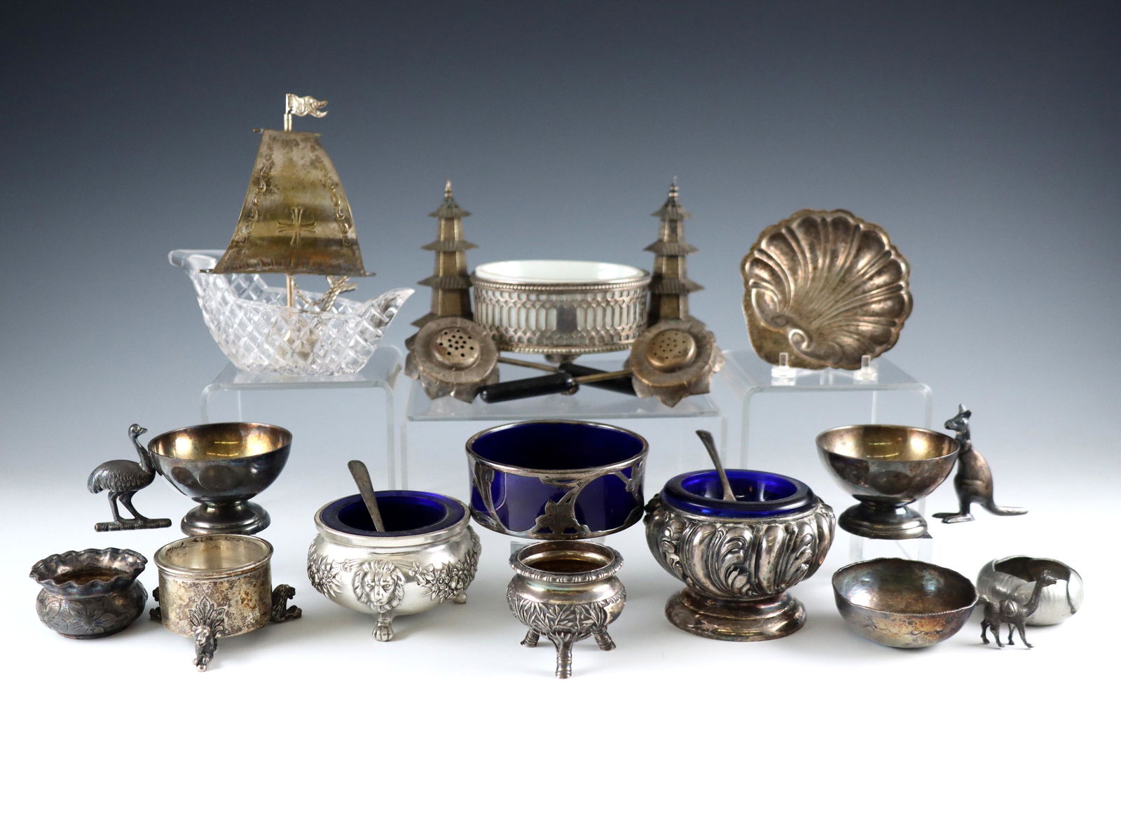 Silverplate Salts & Shakers: A group of Silverplate salt cellars and shakers. Various figural forms including a ship, shell, pagodas, daisies, and animal forms, with four traditional forms having Cobalt Blue and Milk Glass liners