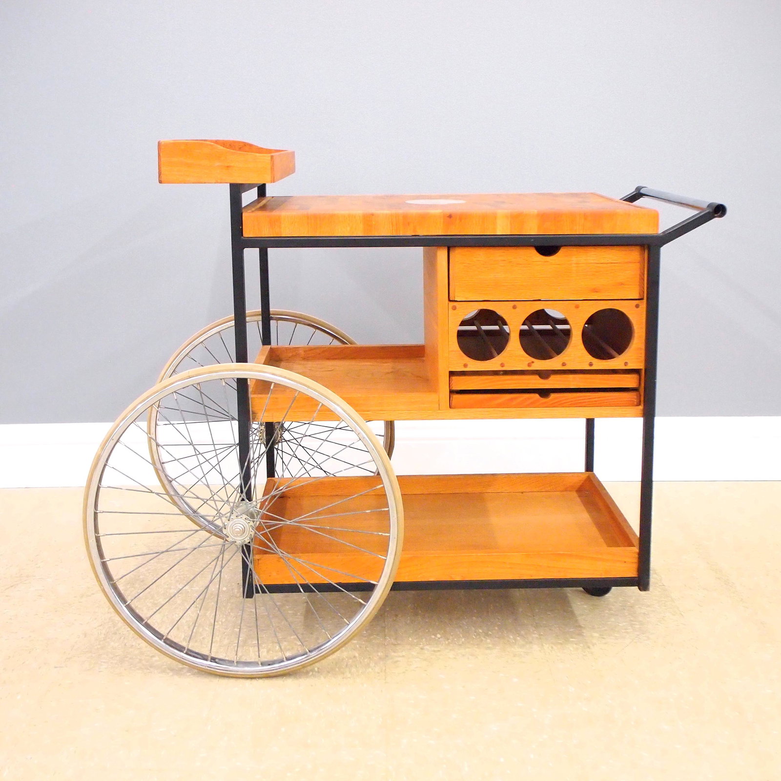A. Umanoff Bar Cart: A mid 20th century Arthur Umanoff bar cart. Oak and Iron construction with a butcher block top and raised gallery shelf over three drawers, two shelves and space for wine storage, with two large spoke