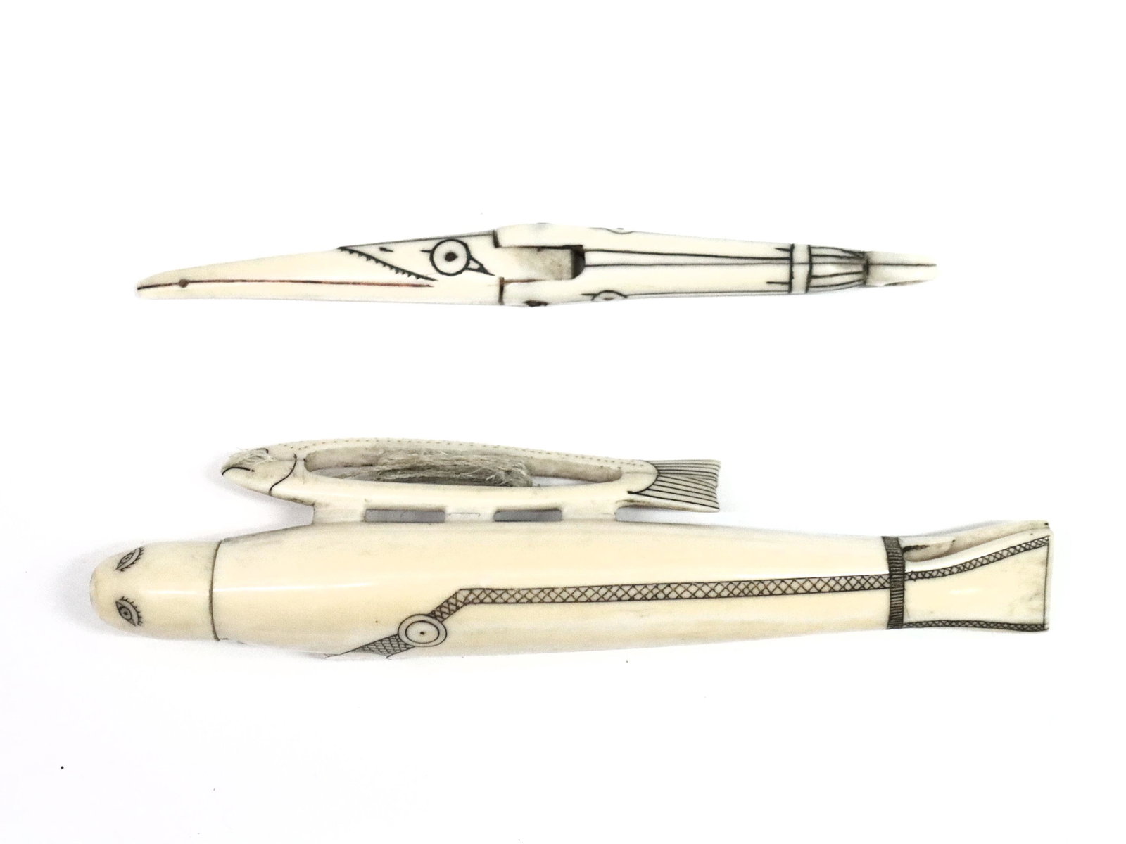 Inuit Carved Bone Sewing Kit: A 19th century Inuit two-piece sewing kit in carved walrus bone with intricate scrimshaw detail. Seal form needle case with stylized fish form bobbin and removable head. Includes a hinged needle with 