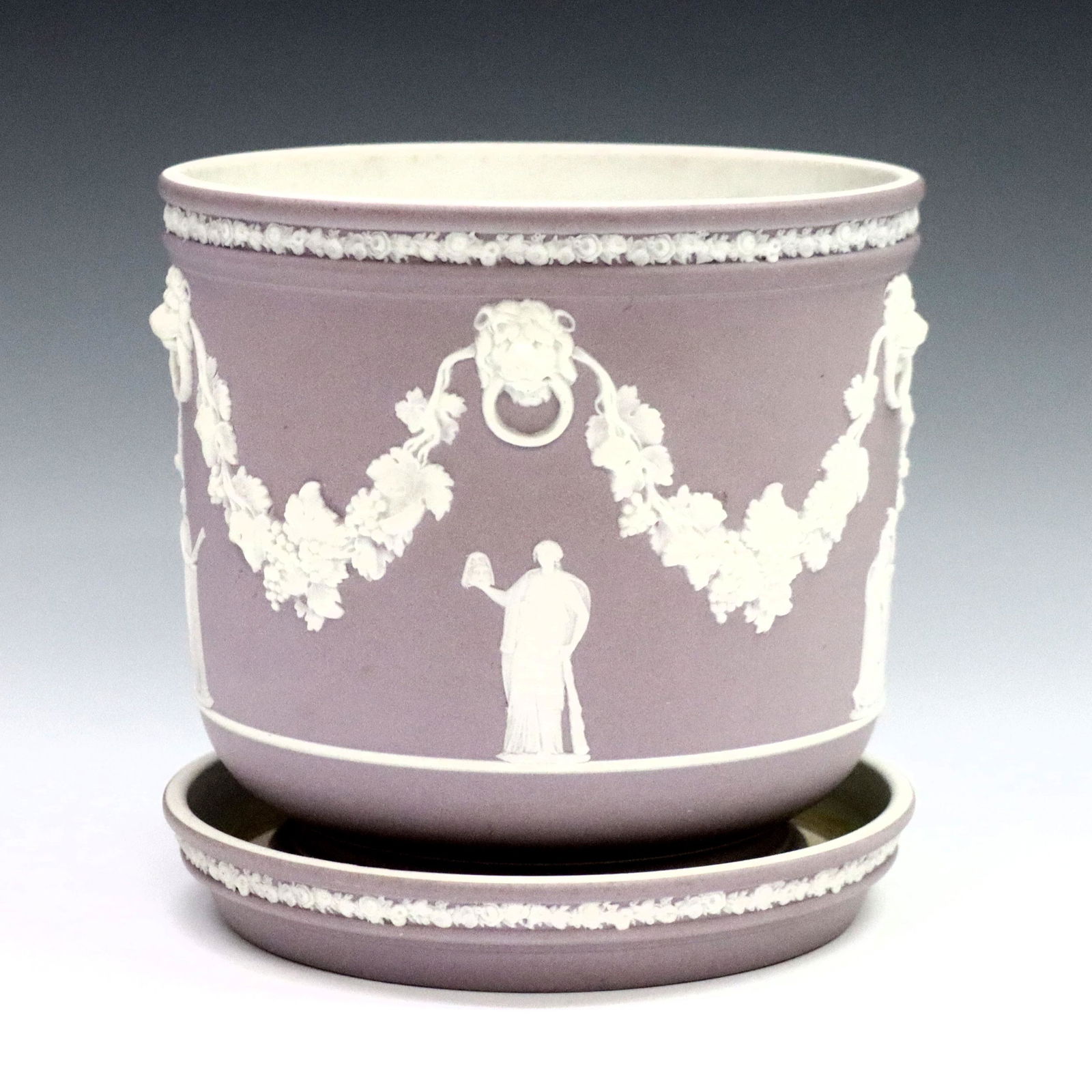 Wedgwood Jasperware Jardiniere: A late 19th century Wedgwood jardiniere with underplate. Lilac Jasper dipped bodies with vintage garlands and classical figures in White relief. Impressed "Wedgwood" and "DRW". Some surface wear and l