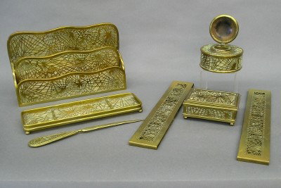 Tiffany Studios desk set: An early 20th century Tiffany Studios "Pine Needle" desk set. Includes a letter rack, pen tray, letter opener, stamp box, round inkwell and blotter ends. Worn gilded finish, letter rack bent with brok