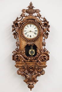 P Haas Carved Wall Clock: A late 19th century carved German wall clock by Philip Haas & Sohne. 8-day spring driven time only movement with painted metal dial and Roman numerals. Carved Walnut case with urn finial and the motto