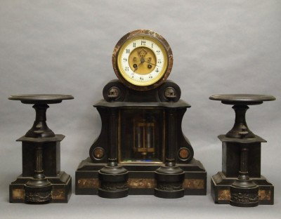 French clock set: A turn of the century French Slate three piece clock set. 8-day time and strike movement with open escapement and porcelain chapter ring. Slate case and garnitures with Brass and marble detail. Edge c