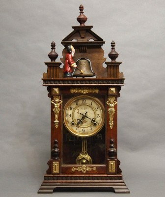 German mantle clock: A turn of the century German mantle clock. 8-day time and strike movement with figural strike on top of case. Walnut case with single door and Brass detail. Restored crown, figure repainted. 27" high.