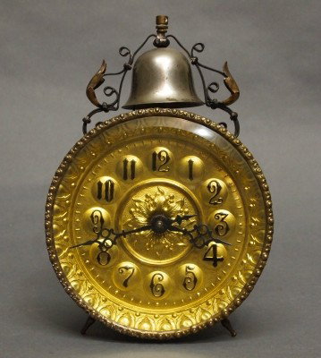 German alarm clock: A turn of the century German alarm clock. Pressed steel case a 30 hr time and alarm movement with bell on top and embossed Brass dial. Some wear. 9" high. ESTIMATE $50-100