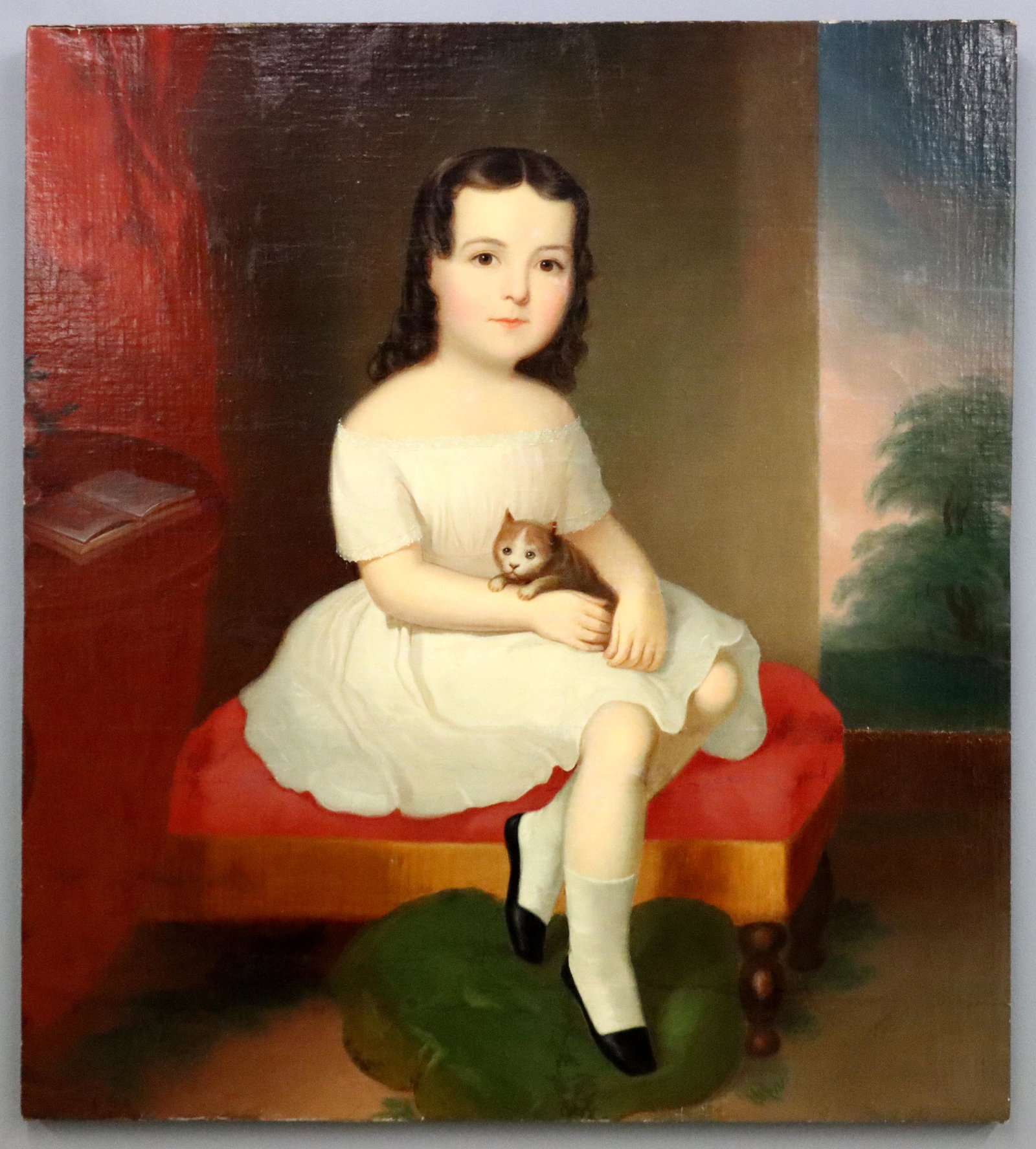American Portrait of a Girl: A mid 19th century American oil on canvas portrait of a girl with kitten. Depicted seated in a Victorian parlor with landscape in the background beyond an open window, unsigned. Canvas cut and lined, 