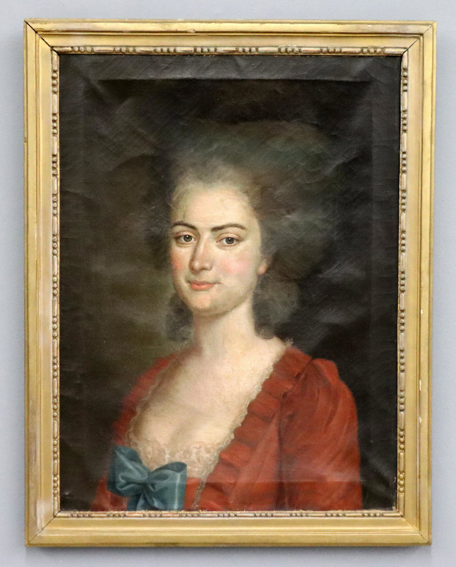 French Portrait of a Lady: An 18th century French oil on canvas portrait of a lady. Depicted quarter length wearing a Red dress with Blue bow, unsigned. Repairs to canvas at face with in-painting, craquelure and surface grunge.