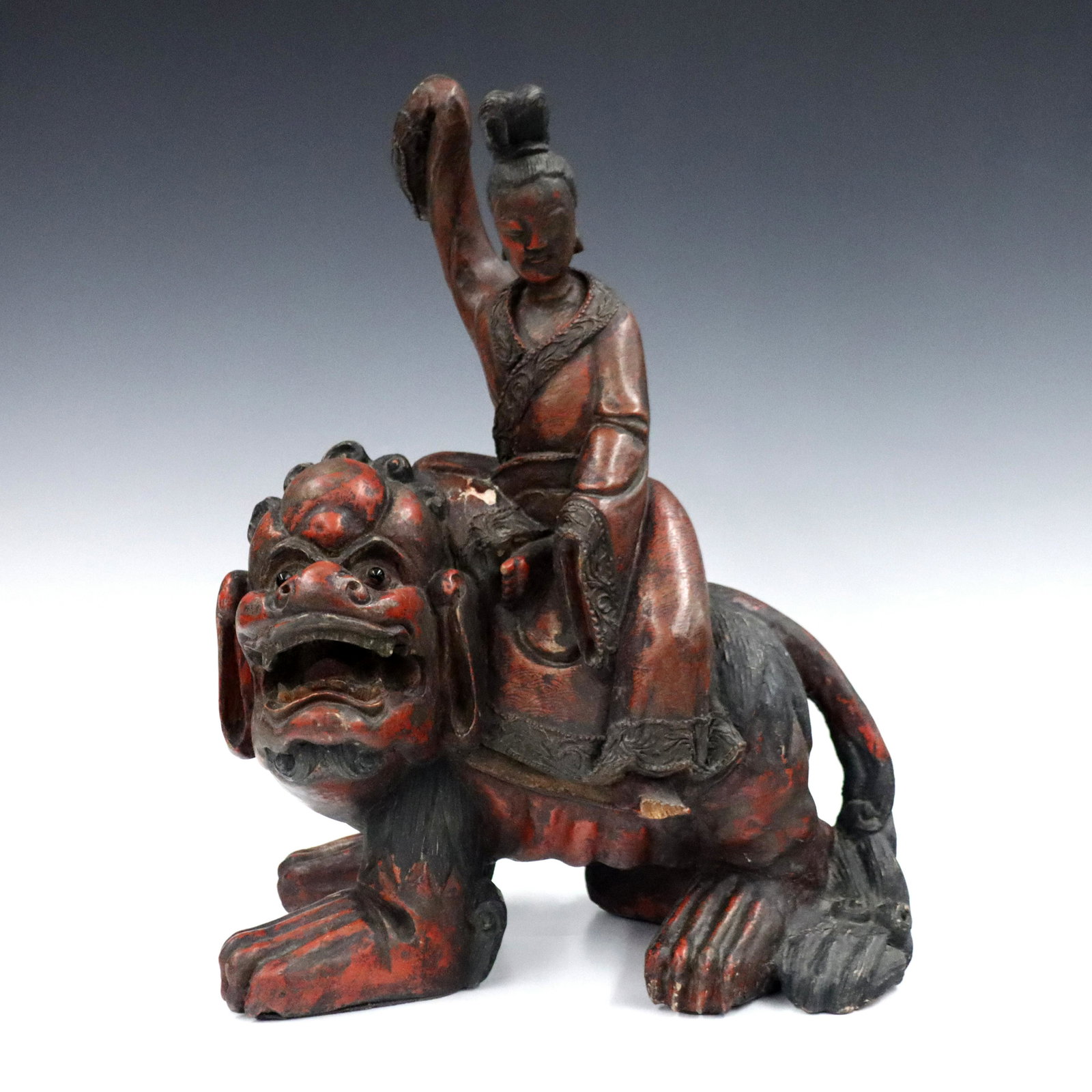 Chinese Carved Guanyin: A Chinese carved wood figure of Guanyin. Depicted seated on a Foo Dog with inset glass eyes and Red painted finish. Wear to finish with some flaking, damage to foot. 17" high. ESTIMATE $300-400