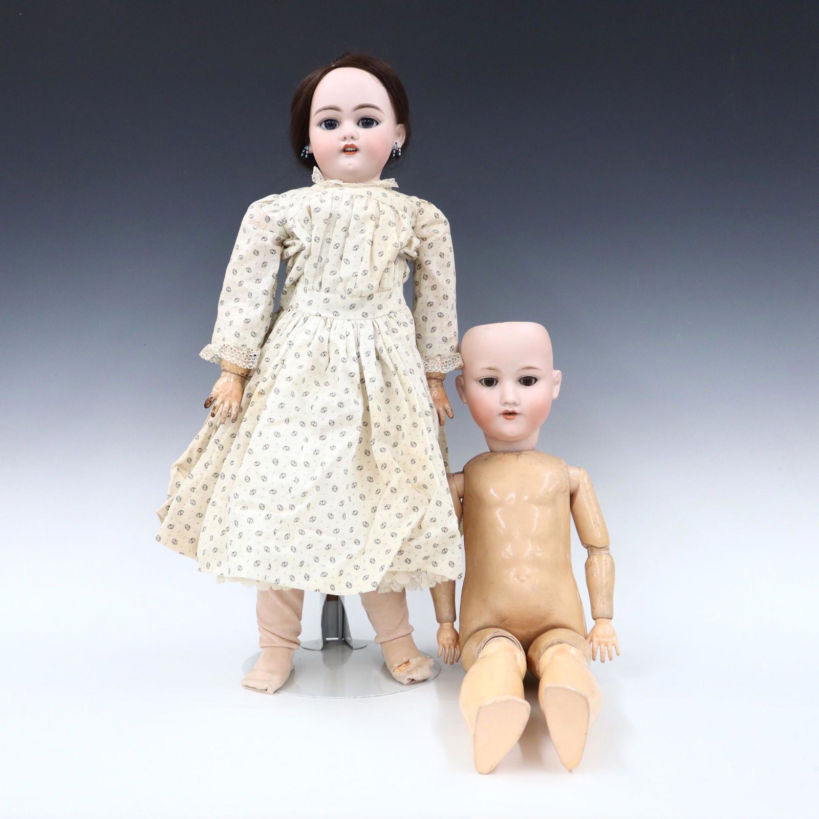 2 German Bisque Dolls: Two turn of the century German dolls. Bisque socket heads with sleep eyes, open mouths with teeth and painted detail on jointed composition bodies. Includes an unmarked doll with pierced ears wearing