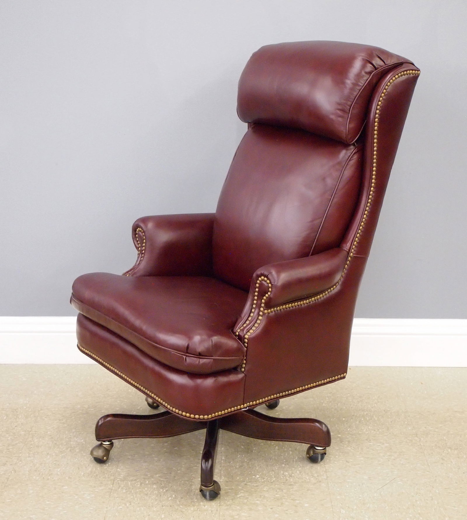 Hancock & Moore Desk Chair: A Hancock & Moore leather desk chair. Upholstered in Burgundy leather with Brass tacks on a Mahogany swivel base with rollers. Minor wear. 46" high. ESTIMATE $400-600