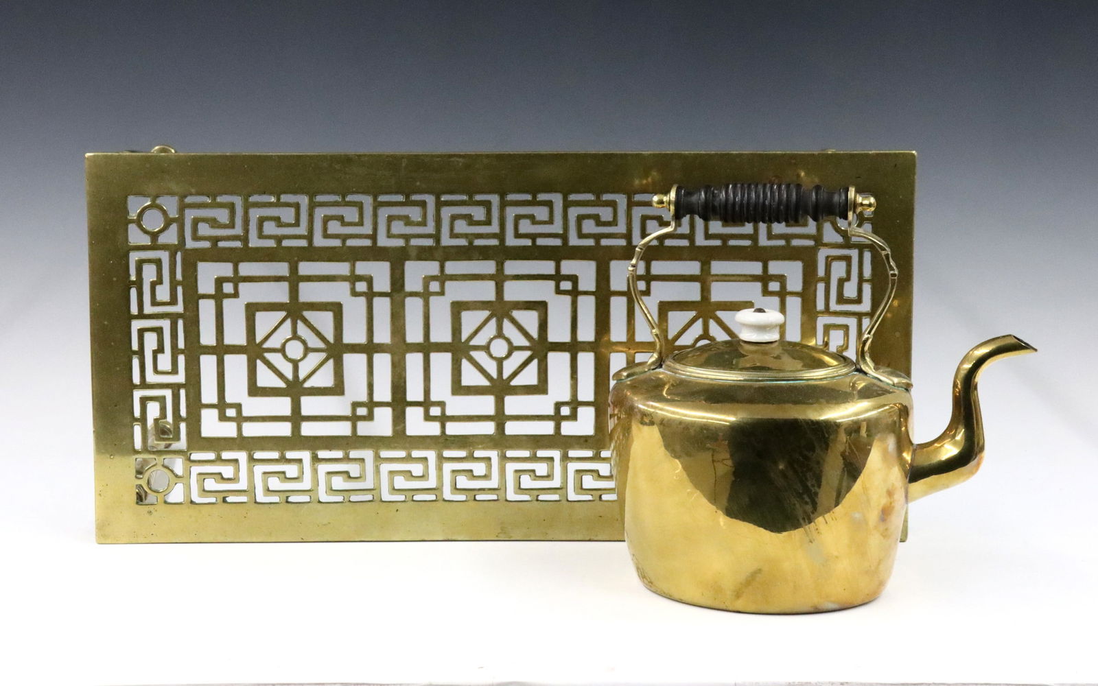 Brass Trivet & Teapot: A turn of the century Brass trivet and teapot. Includes a trivet with pierced top and tall legs, with a Brass and Copper teapot marked "S & S". Some surface wear and pitting. Trivet is 18 1/2 x 9 x 9"