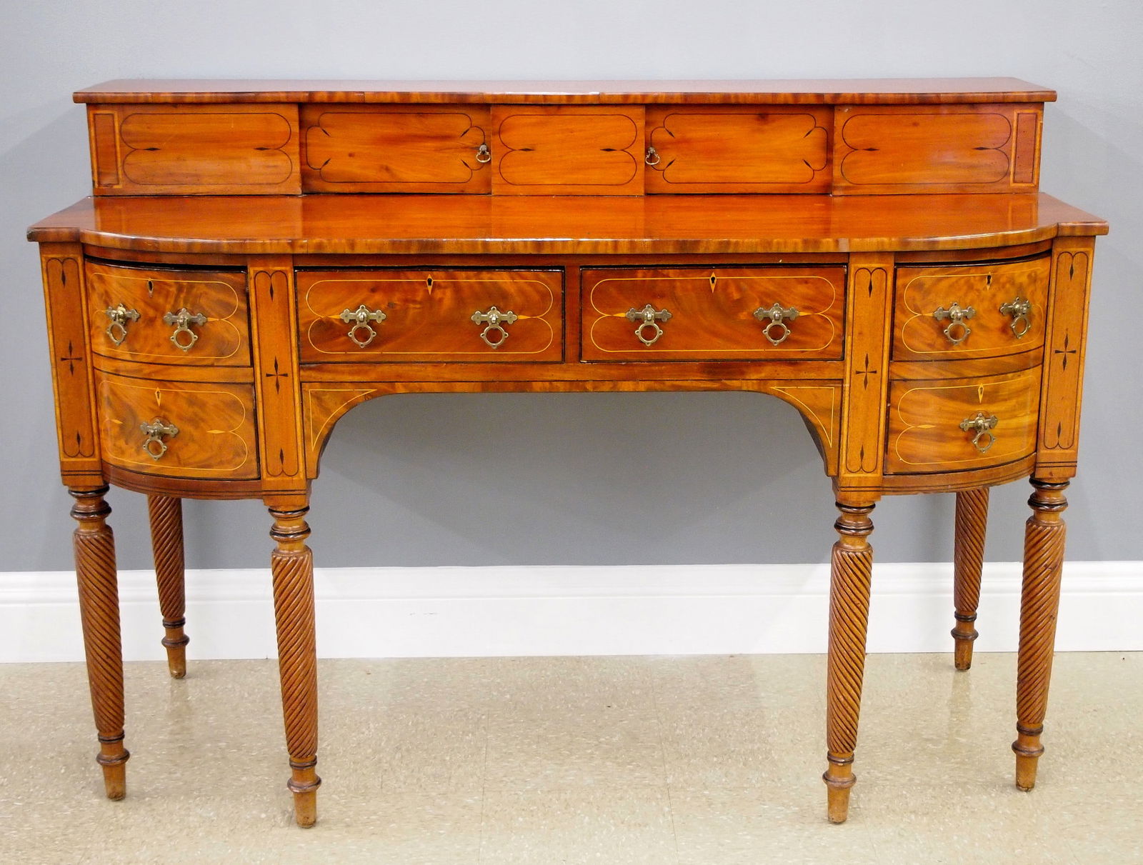 English Regency Sideboard: An early 19th century English Regency Period sideboard. Figured Mahogany construction with contrasting Ebony and Boxwood inlay features a shaped facade with upper display shelf and sliding doors over