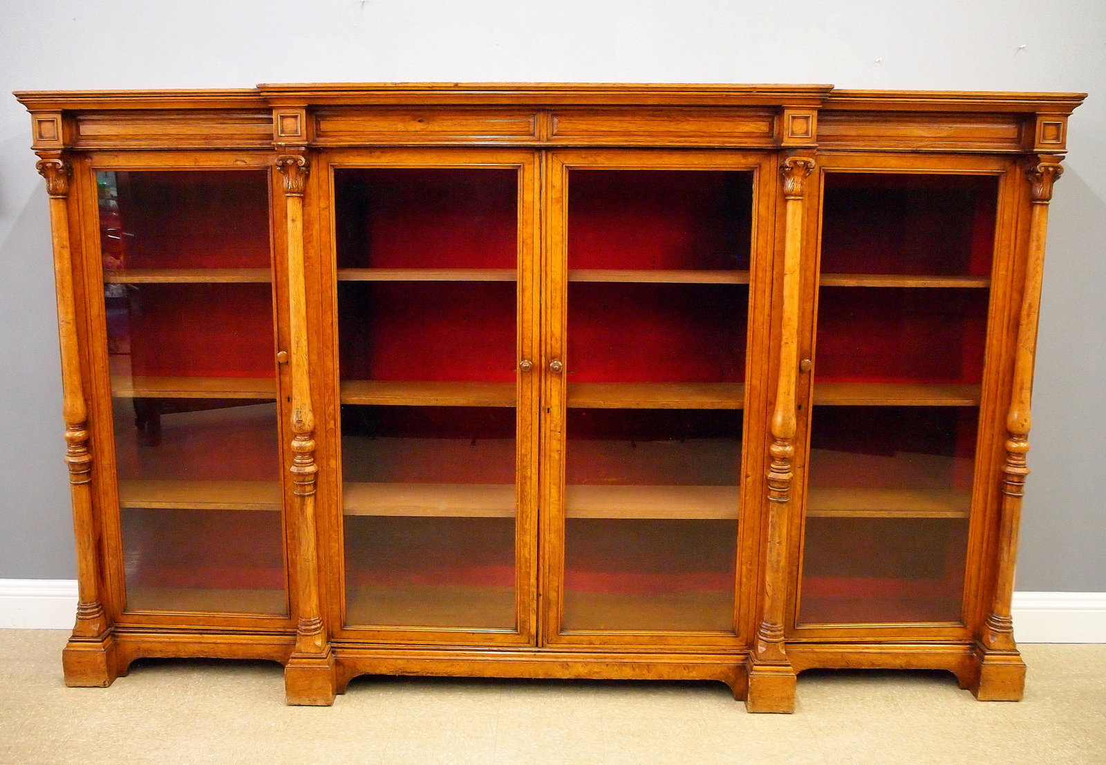 English Victorian Library Case: A 19th century English Victorian Period breakfront library case. Oak construction with a molded cornice over four glazed doors flanked by turned columns on a stepped plinth base with simple arched det