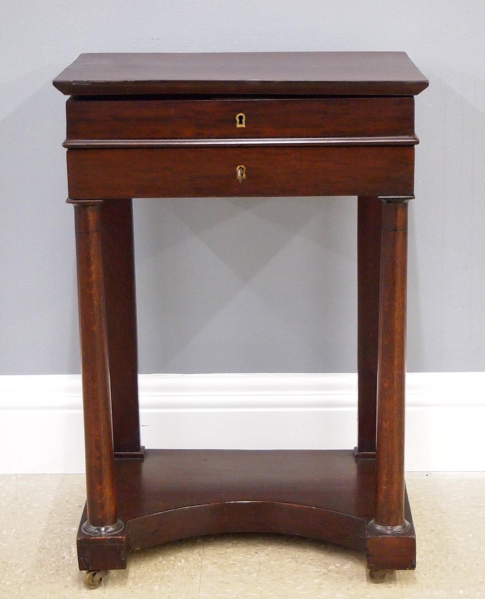 French Empire Period Sewing Table: A 19th century French Empire Period sewing table. Mahogany construction with shaped top, single drawer and round tapered front legs on a shaped platform base. Hinged top opens to reveal a mirrored lid