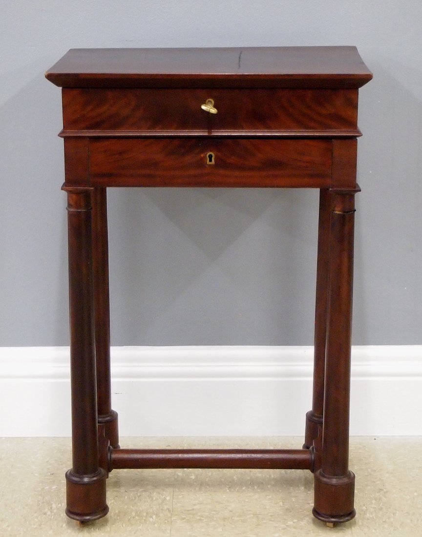 French Empire Style Sewing Table: A 19th century French Empire style sewing table. Mahogany construction with shaped top, single drawer and round tapered legs on a shaped stretcher base with turned feet. Hinged top opens to reveal a m