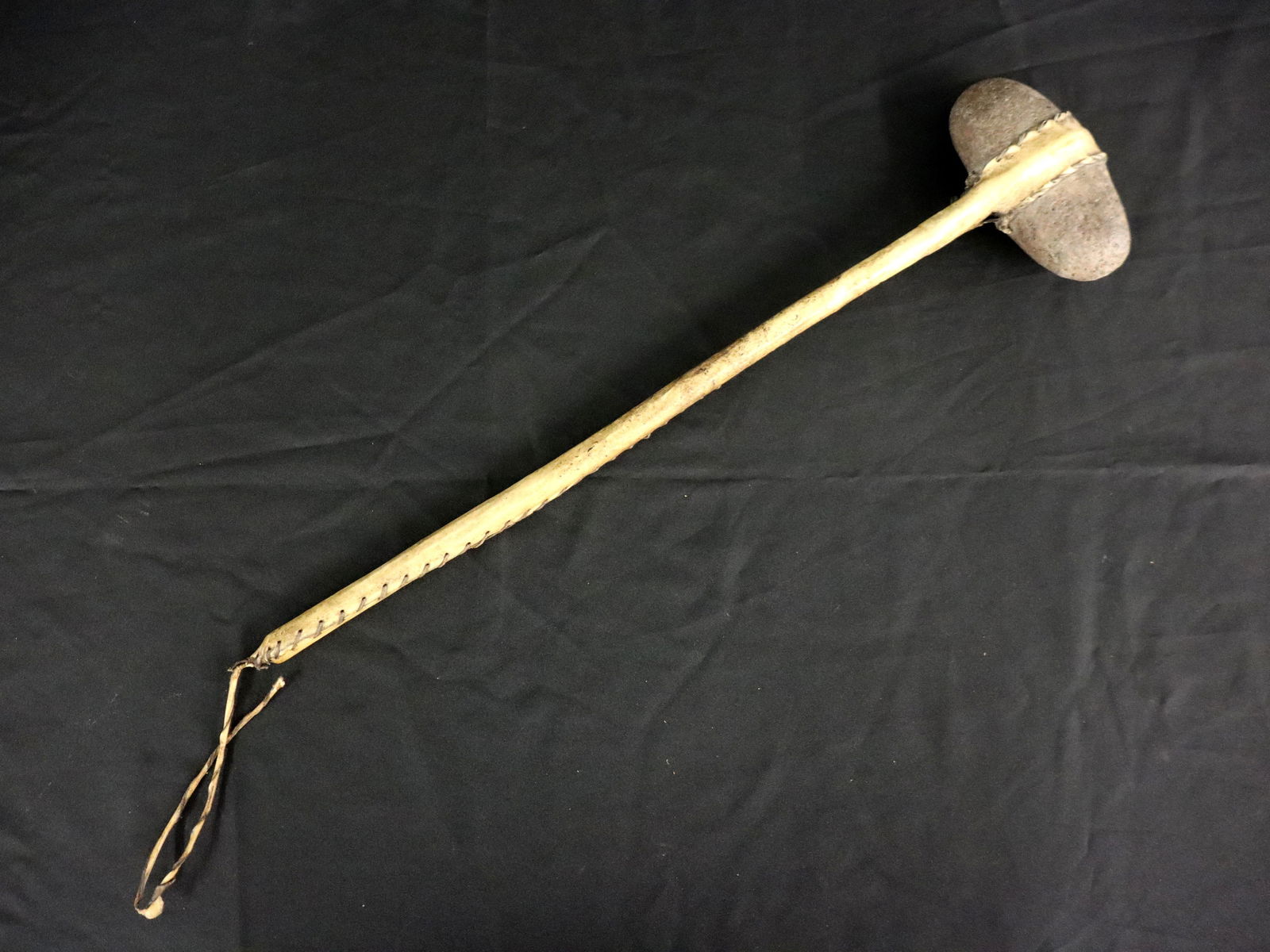 Native American War Club: A turn of the century Native American stone war club. Oval stone head secured to a wooden shaft with sewn hide. Some wear. 22" long. ESTIMATE $300-400