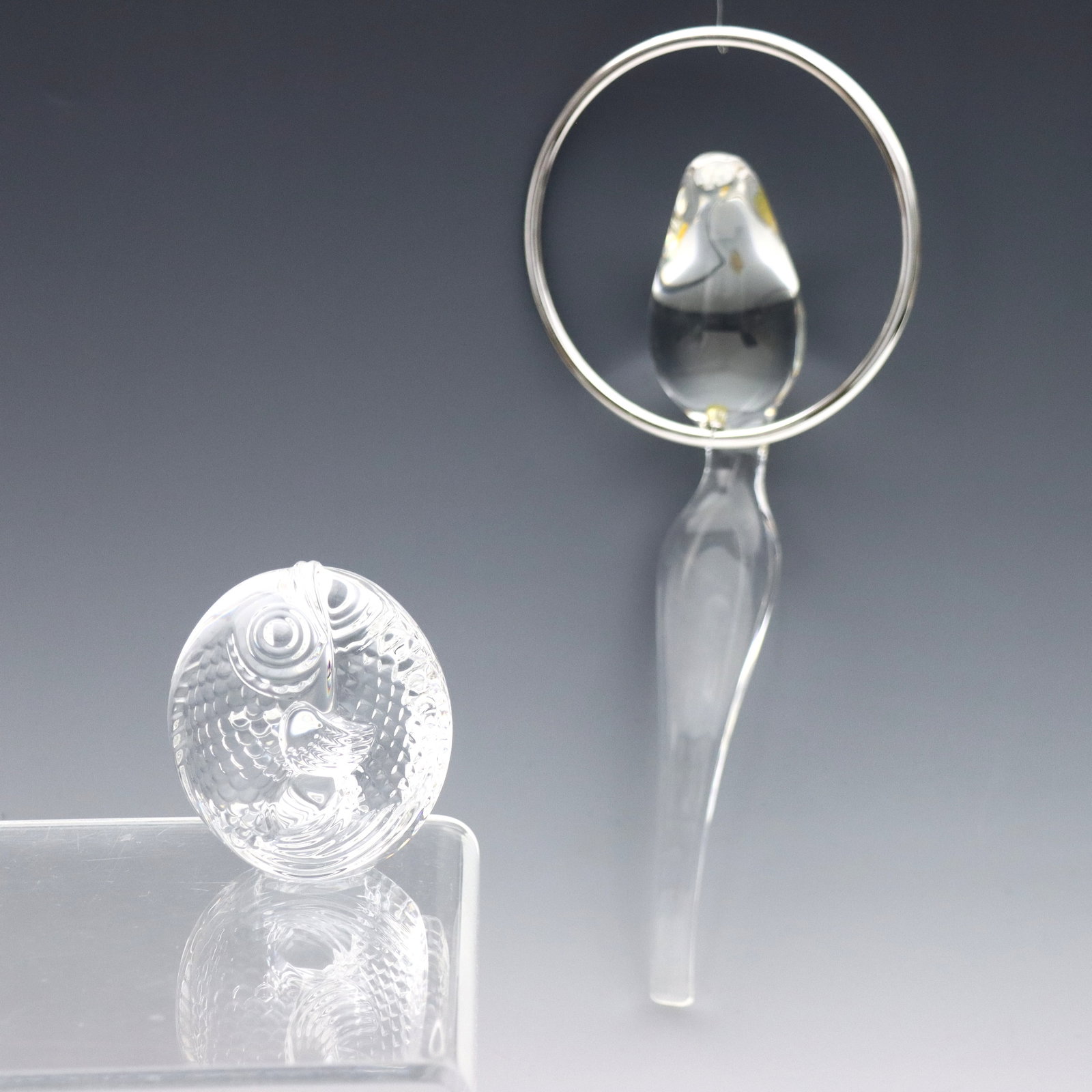 2 Steuben Crystal Animal Figures: Two mid 20th century Steuben Crystal animal figures. Includes a "Bird on a Perch" ornament with Sterling Silver hoop, and an entwined "Koi" hand cooler. Etched "Steuben" signatures, hoop impressed "ST