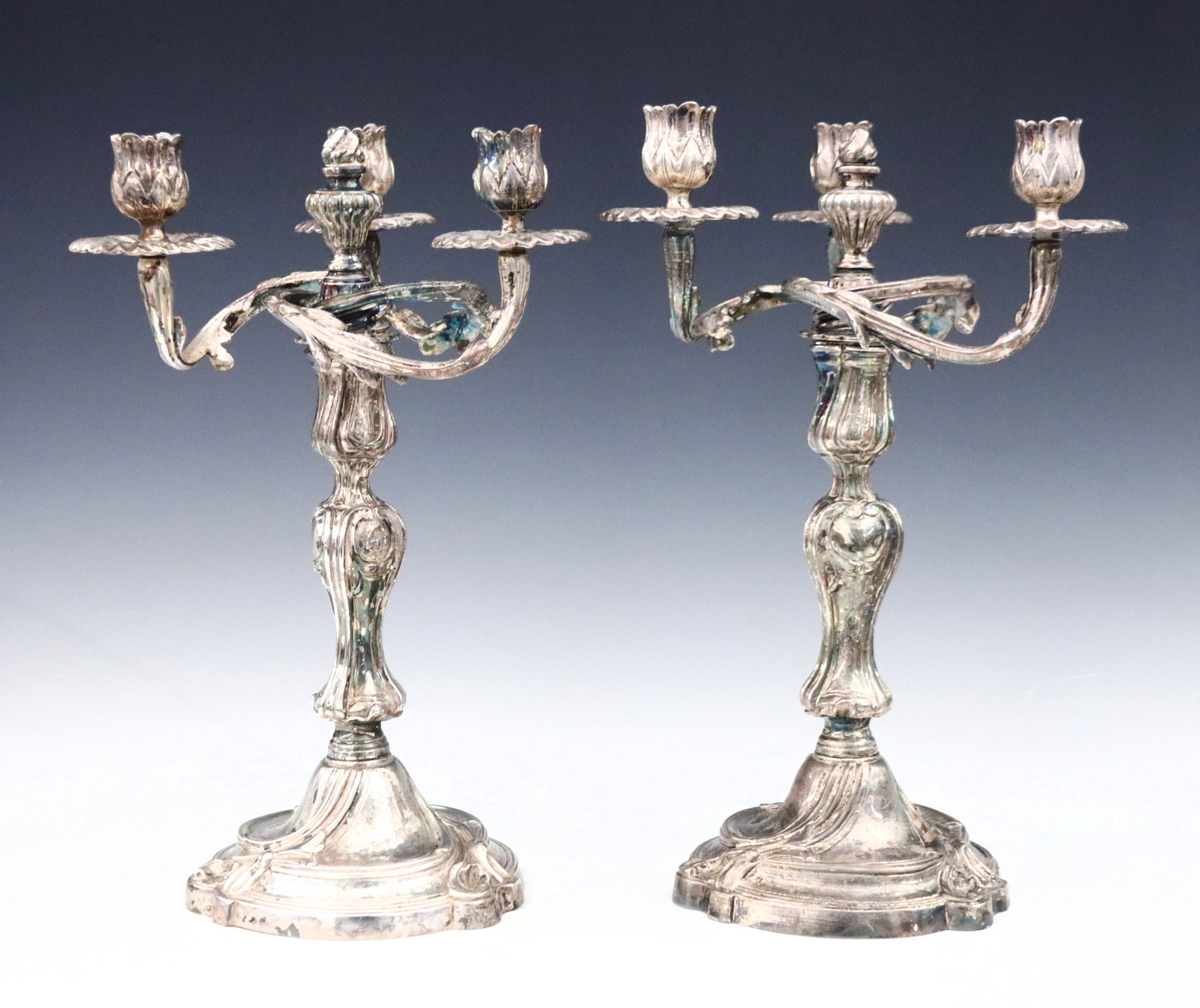 Pr French Silverplate Candelabra: A pair of 19th century French Rococo style Silverplate candelabra. Features three scrolled foliate arms surrounding a central finial over a baluster stems and circular base with engraved decoration. E