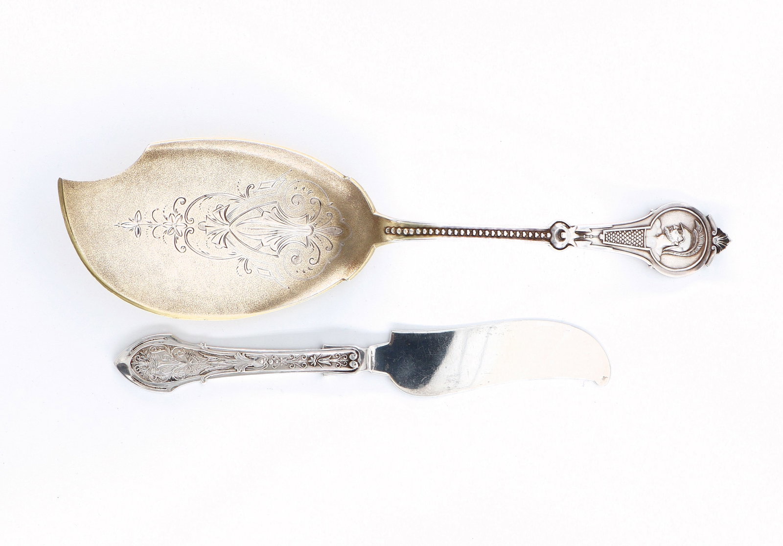2 pc W & H Sterling Flatware: Two pieces of late 19th century American Sterling Silver flatware by Wood & Hughes. Includes a "Warrior" pattern Medallion dessert server with engraved decoration and gold wash blade, and a "Angelo" p