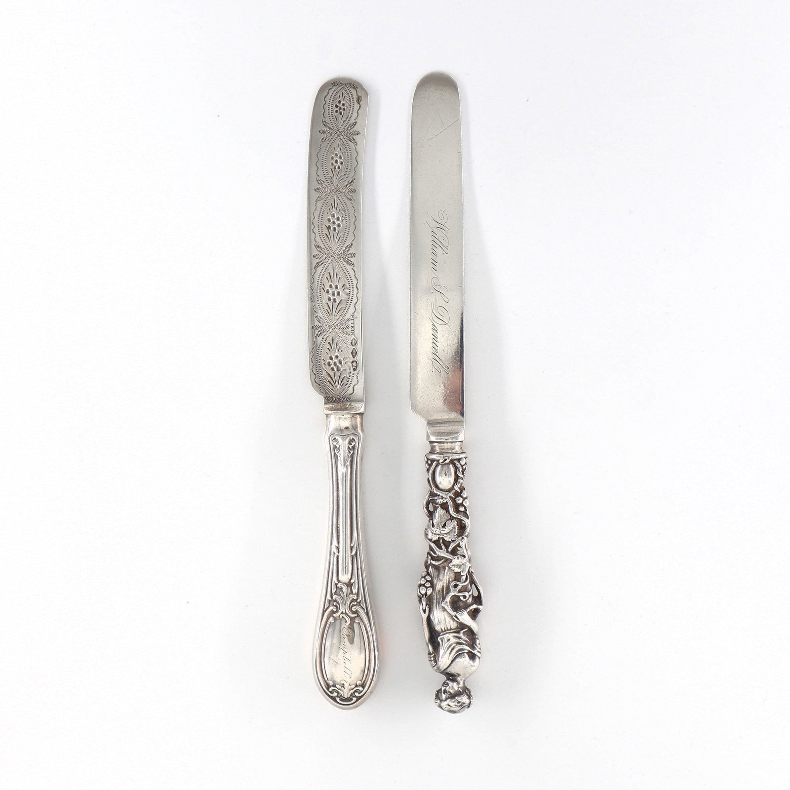 2 American Coin Silver Master Butter Knives: Two mid 19th century American Coin Silver master butter knives, New York. Includes a figural knife depicting a Neoclassical woman with grapes by Ball Black & Co. and William Forbes, c. 1840, and a hol