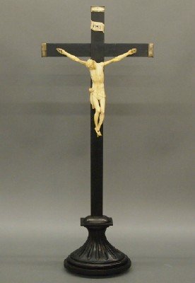 Carved Crucifix: A turn of the century carved Bone Crucifix on a wooden cross with Brass end caps on a fluted stand. Some wear, hairlines in figure. 28 1/2" high overall. ESTIMATE $200-300