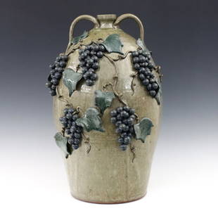 M. Crocker Folk Art Stoneware Jug: Michael Crocker, American (Georgia), b. 1956. A contemporary Stoneware Folk Art jug. Two strap handles and applied Grape Vine decoration with polychrome glaze on a mottled Green ground. Signed "Michae