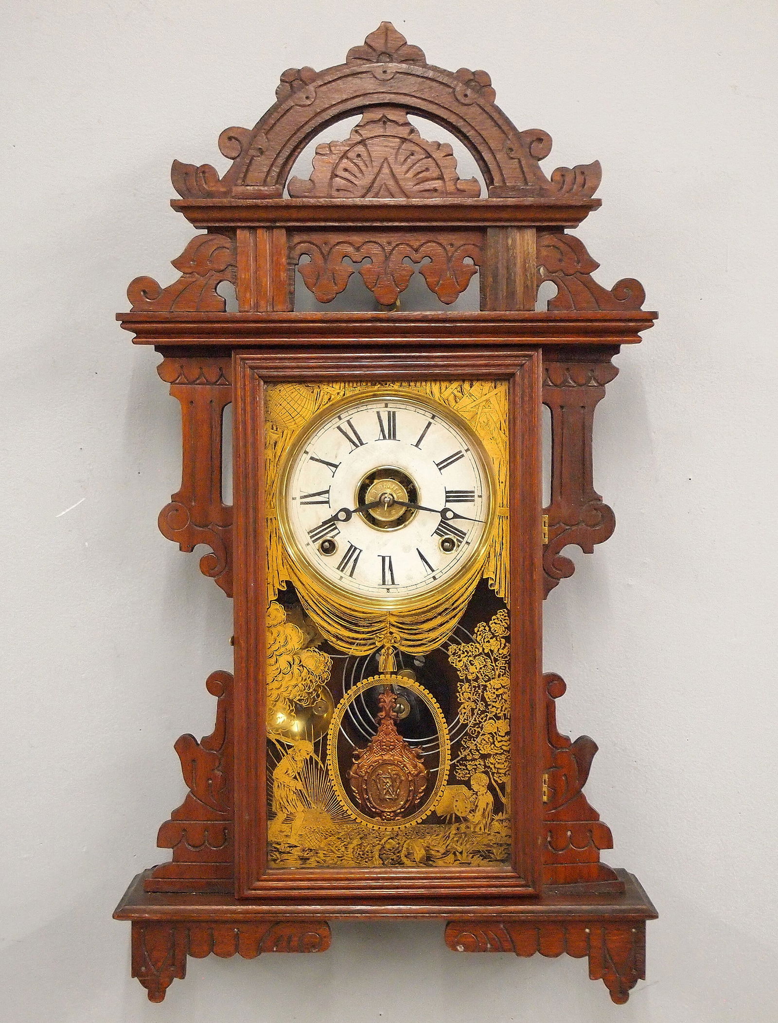 Welch Donita Kitchen Wall Clock: A turn of the century E. N. Welch Donita model kitchen wall clock. 8-day time, strike and alarm movement with papered metal dial and Roman numerals. Walnut case with cutout crest over a single door wi