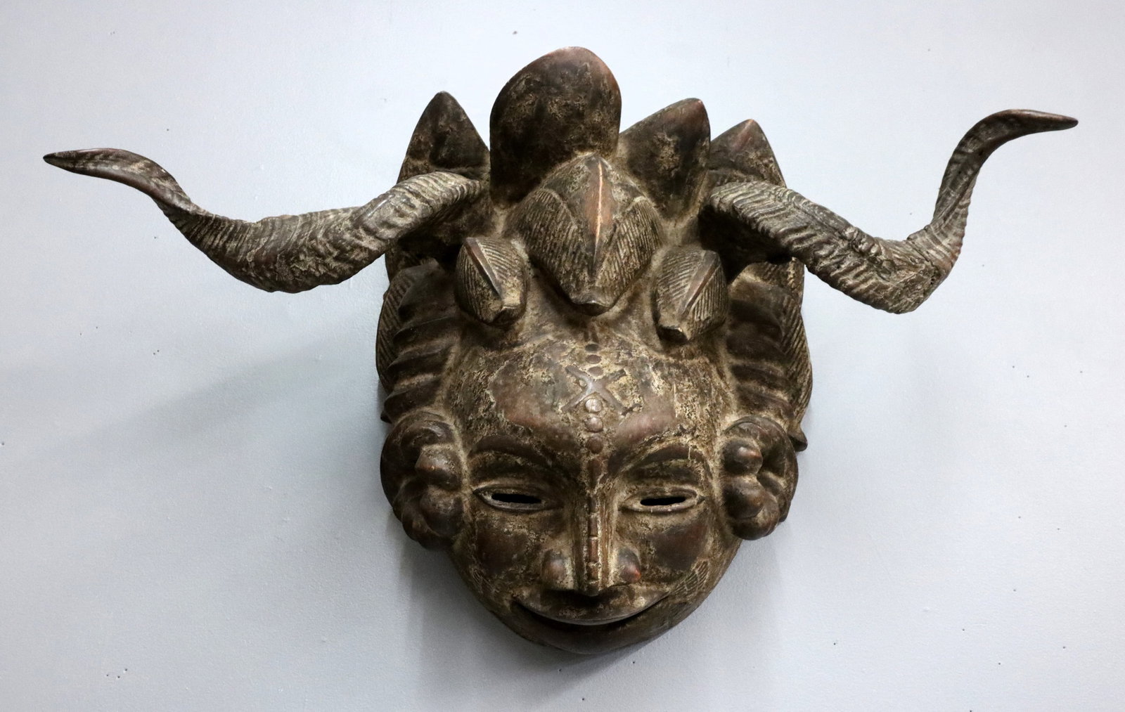 Cameroonian Carved Buffalo Mask: An Cameroonian Bamum culture carved wooden Buffalo mask with spiraled horn. Wear and some damage, shrinkage. 18" high. ESTIMATE $200-400 NOTE: From the collection of Fred Brown, Brighton, Michigan. Pu