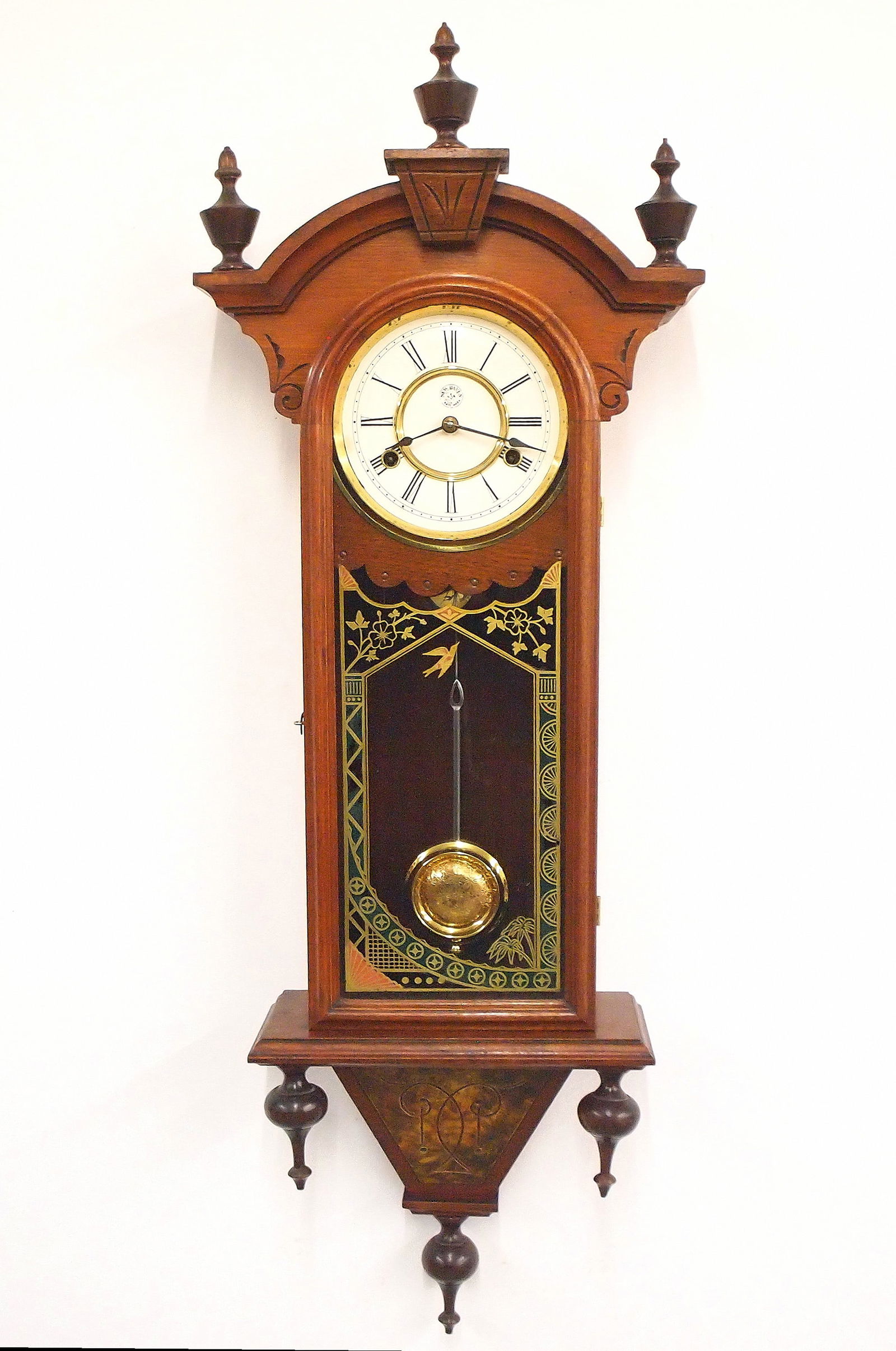 New Haven Winnipeg Model Wall Clock: A late 19th century New Haven Winnipeg model wall clock. 8-day time and strike movement with a papered metal dial and Roman numerals. Walnut case with arched crest and turned finial over an arched mol