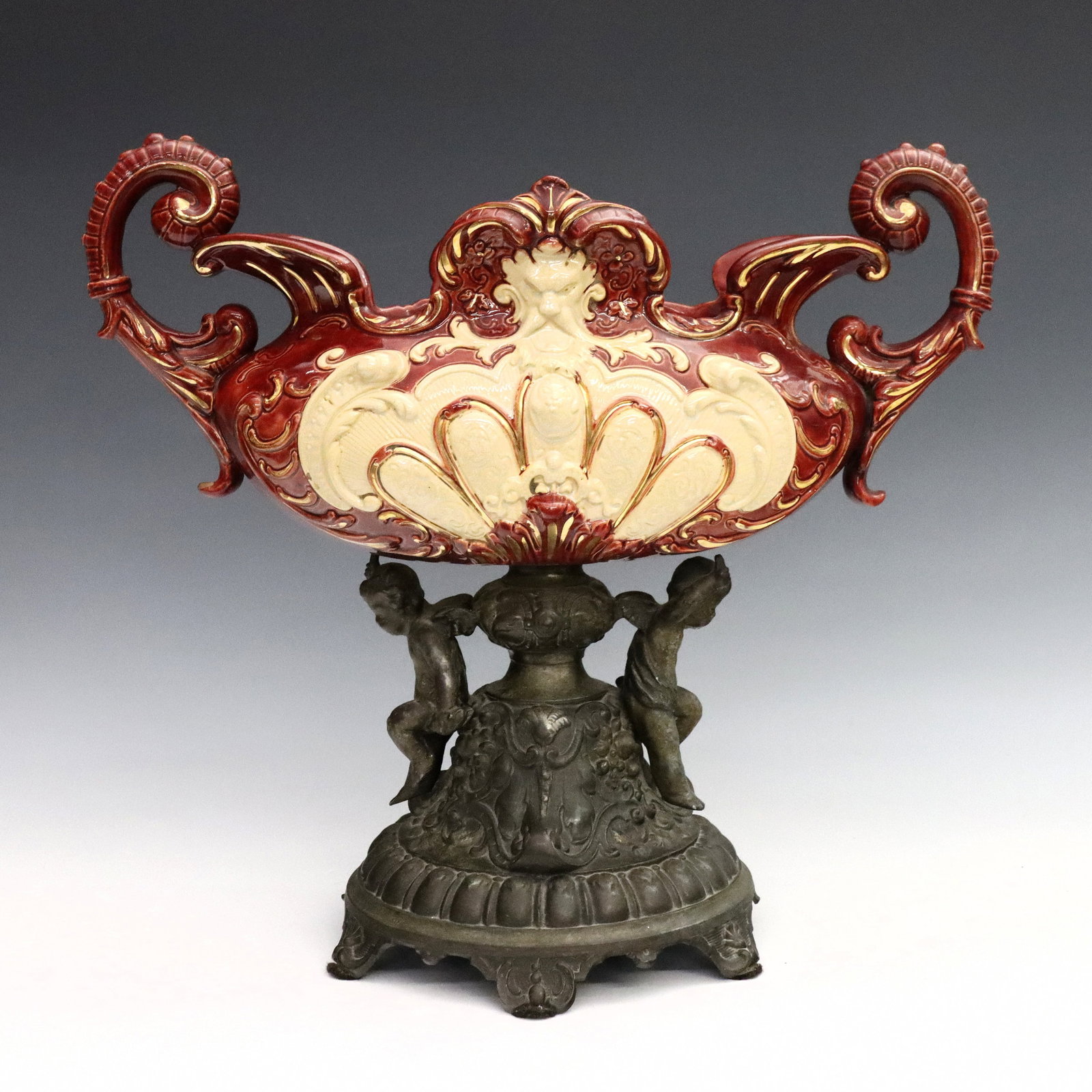 Rococo Revival Majolica Centerpiece: A late 19th century Rococo Revival Majolica centerpiece. Oval bowl with scrolled handles, Neoclassical design and Gilded detail on a Spelter pedestal base with cast Cherubs at the stem. Bowl impressed