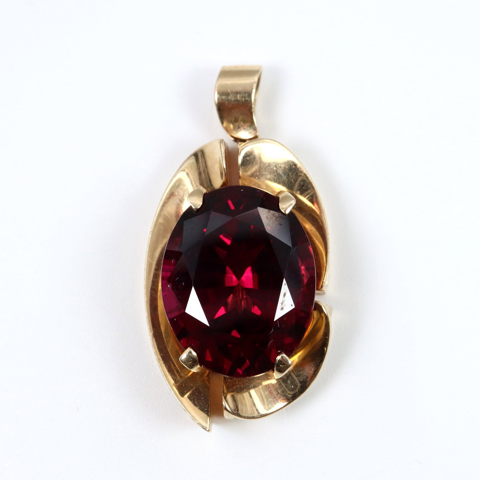 14k Gold & Rhodolite Pendant: A 14k Gold and Rhodolite Garnet pendant. Features an oval cut prong set Garnet approx. 10 1/2 x 16 mm, on a scrolled pendant with openwork design. Marked "14k" and "FYKim" maker's mark, attributed to 