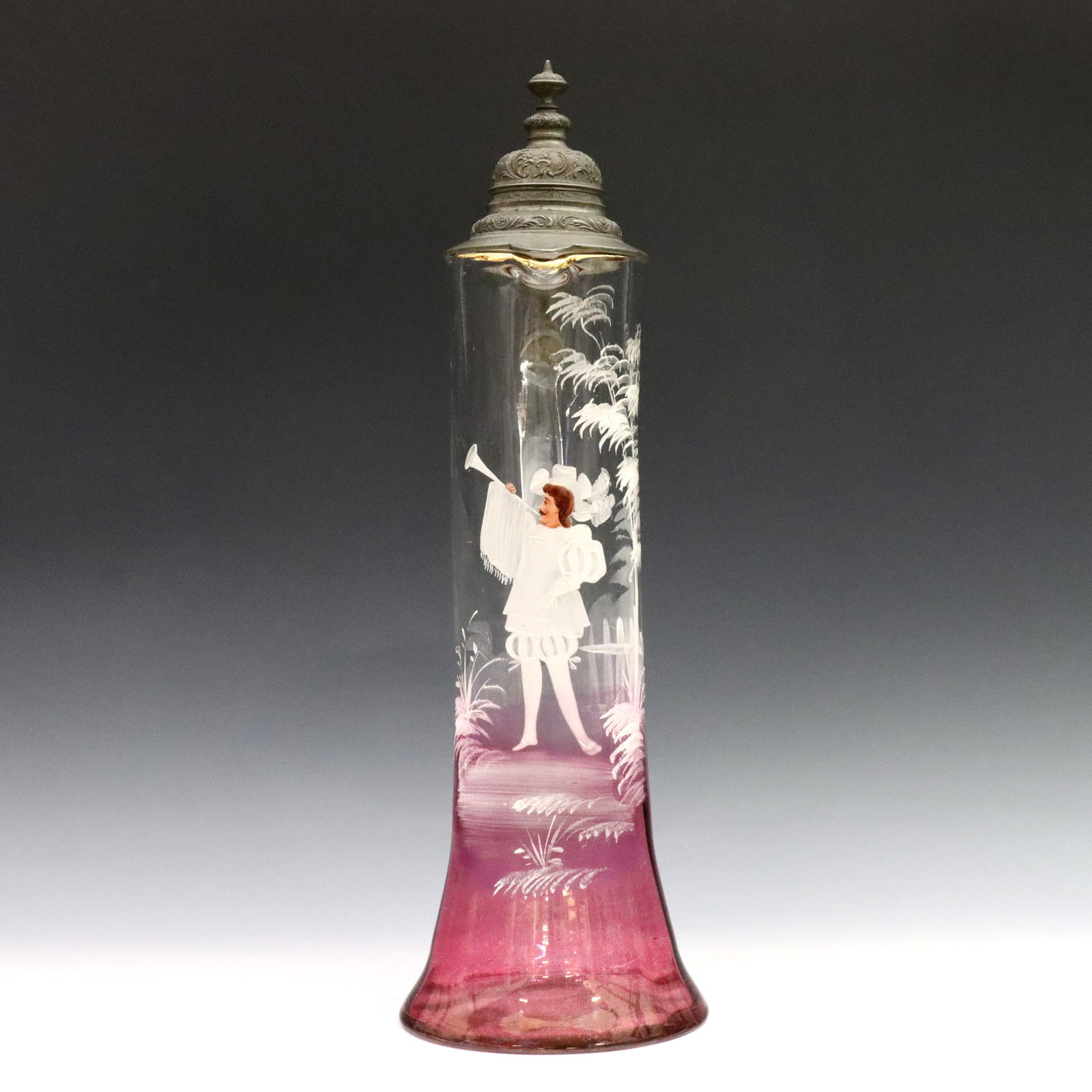 Mary Gregory Flagon: A late 19th century Mary Gregory Art Glass flagon. Tapered form in clear to Cranberry glass with flared foot, hinged pewter lid and enameled figural court decoration. Minor surface wear, lids sits ask