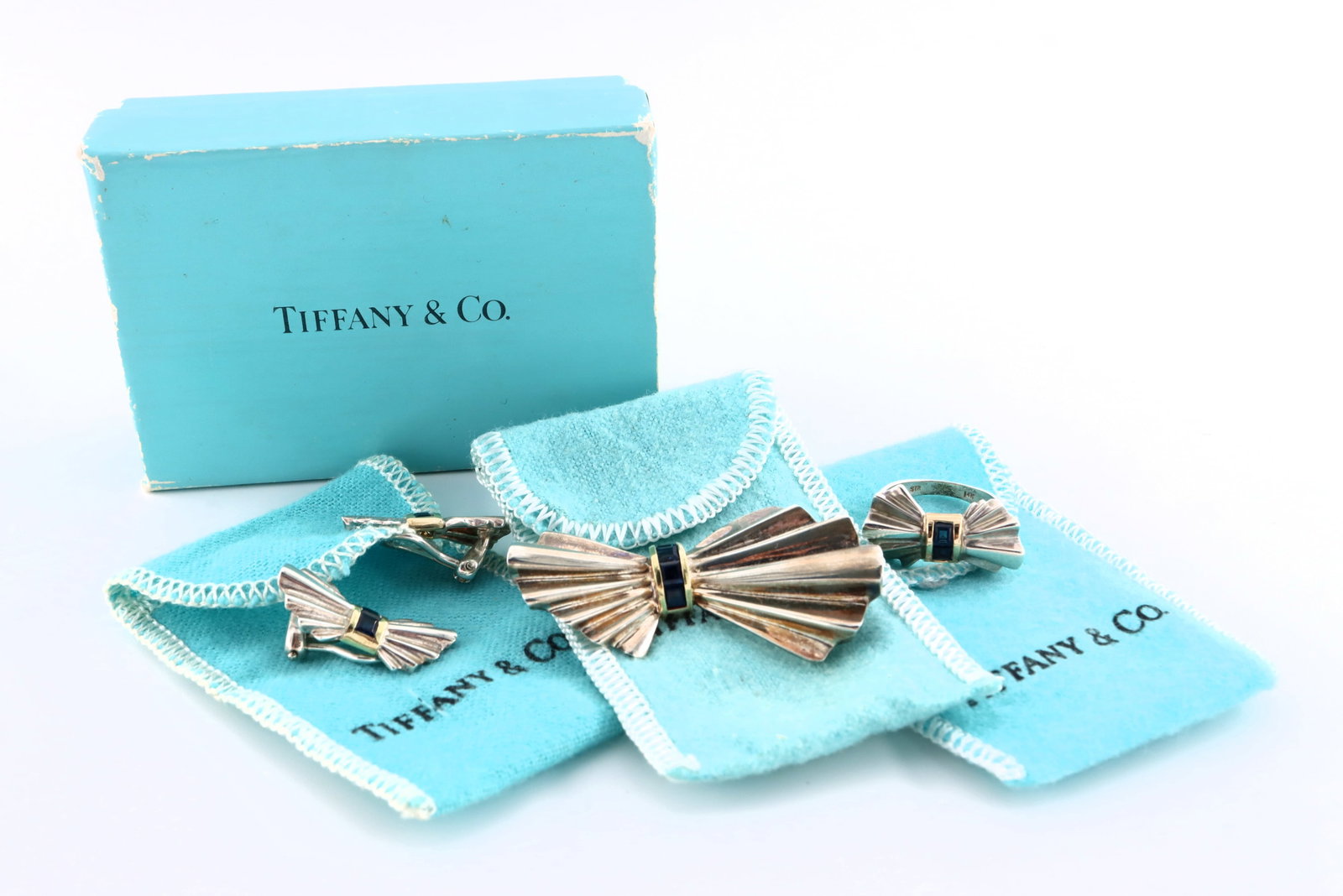 3 pc Tiffany Sterling & Gold Bow Jewelry: Three pieces of Tiffany & Co. Sterling Silver and 14k/18k Gold jewelry. Features Sterling bow forms with square cut Sapphire stones in a 14k or 18k Gold bezel setting. Includes a brooch, pair of clip-