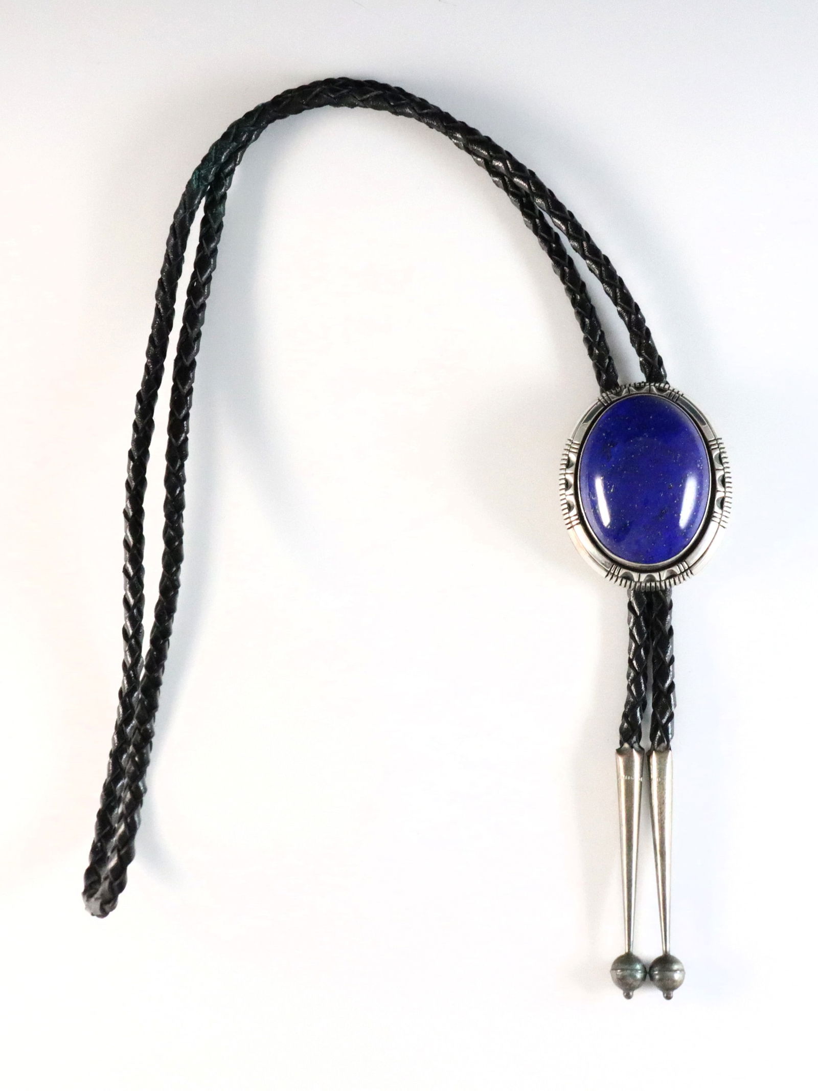 W.J. Johnson Navajo Sterling Bolo Tie: A vintage Navajo Sterling Silver bolo tie by William J. Johnson. Features an oval clasp with bezel set Lapis Lazuli stone and reeded detail on a braided leather tie. Marked "W.J. Johnson / Sterling".