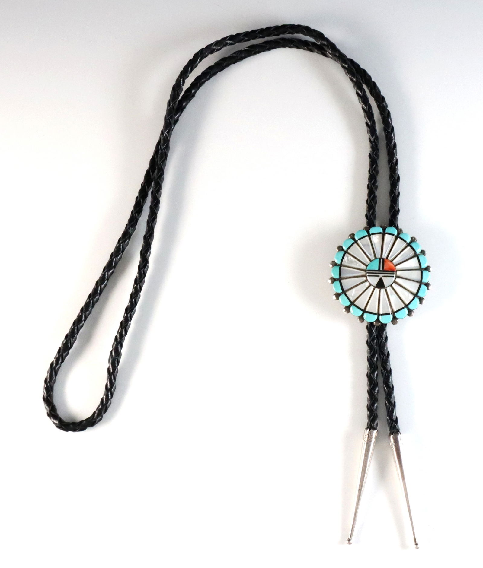 D.V. Hattie Zuni Sterling Bolo Tie: A vintage Zuni Sterling Silver bolo tie by Derrick and Vivian Hattie. Features a circular Sun Face clasp with inlaid Turquoise, Coral, Jet and Mother of Pearl on a braided leather tie. Marked "D.V. Ha
