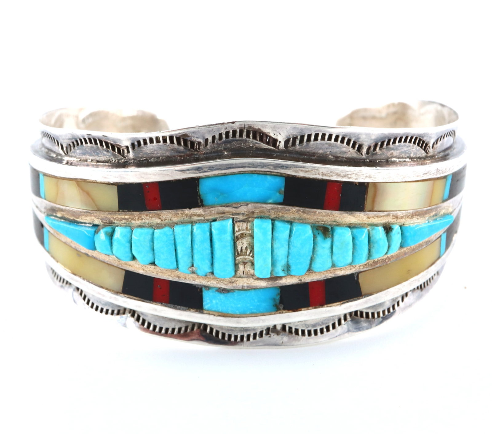 Zuni Wayne Paquin Sterling Cuff: A vintage Zuni Sterling Silver cuff bracelet by Wayne Paquin. Wide design with a row of graduated Turquoise stones surrounded by inlaid Mother of Pearl, Coral, Jet and Turquoise with engraved detail.