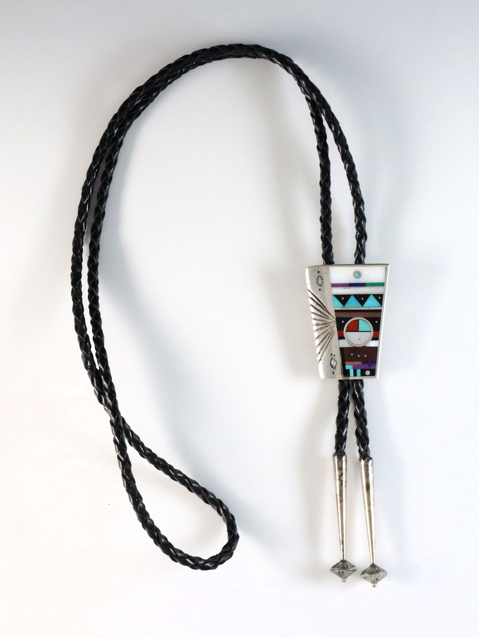 H. Smith Navajo Sterling Bolo Tie: A vintage Navajo Sterling Silver bolo tie by Harold Smith. Features a trapezoidal clasp with geometric design of inlaid Turquoise, Coral, Jet, Mother of Pearl and other stones on a braided leather tie