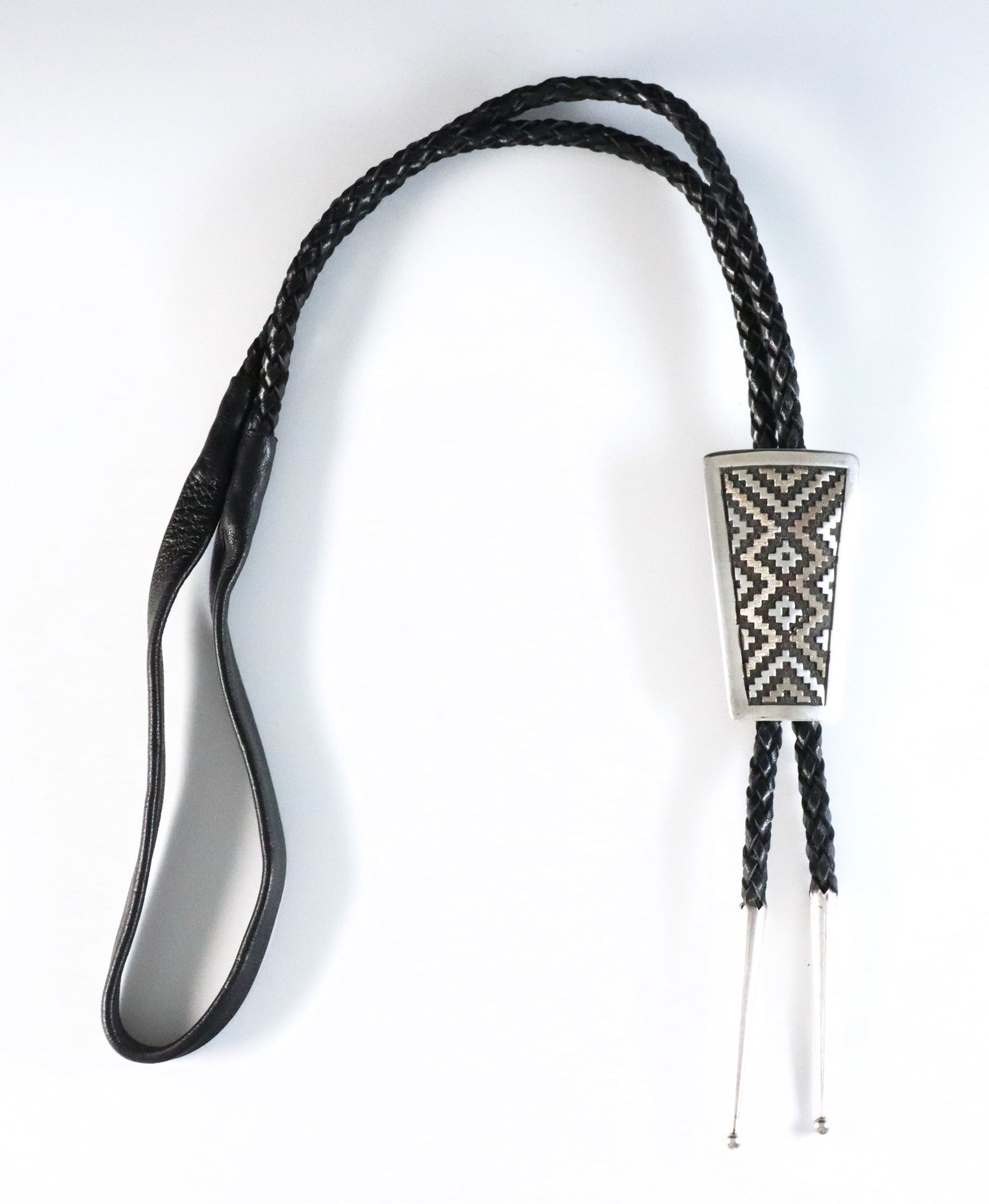 T. Jackson Navajo Sterling Bolo Tie: A vintage Navajo Sterling Silver bolo tie attributed to Tommy Jackson. Features a trapezoidal clasp with geometric design on a braided leather tie. Incised "Jackson", tested Sterling. 1.65 troy ozs to
