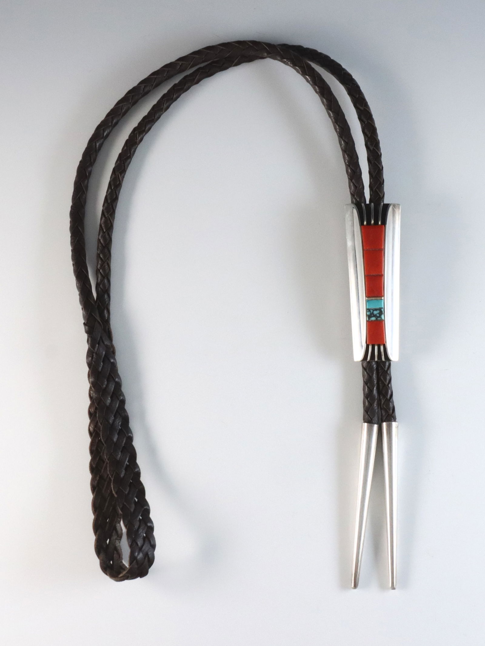 V. Beck Navajo Sterling Bolo Tie: A vintage Navajo Sterling Silver bolo tie by Victor Beck. Features a rectangular clasp with fluted design and inset Coral and Turquoise on a braided leather tie. Incised "Victor Beck", tested Sterling