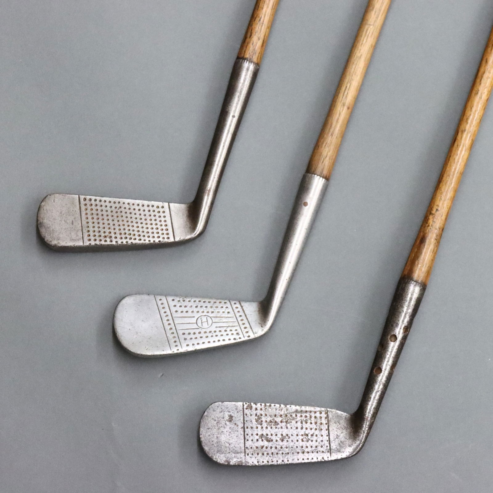3 Scottish Iron Golf Clubs: Three early 20th century Scottish scored face iron golf clubs. Includes a Geroge Nicoll nap putter iron retailed by E. Gray & Co. c. 1910-1920, a James Gourlay putter with Maxwell holes in the hosel c
