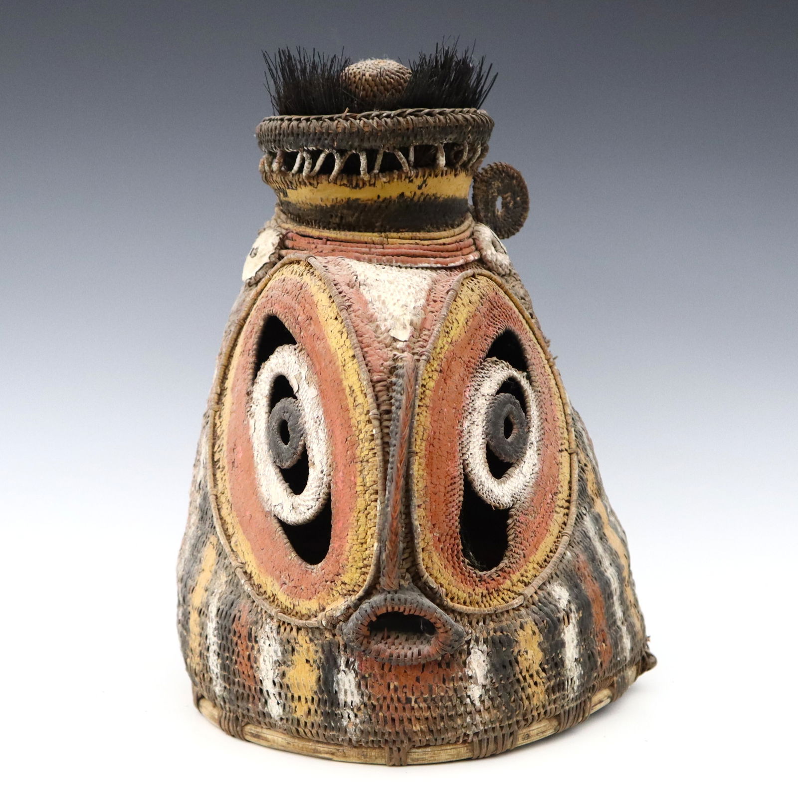 PNG Woven Yam Mask: A Papua New Guinea ceremonial yam mask from the Abelam people, East Sepik Province. Woven fiber mask with polychrome decoration, features concentric oval eyes and pierced mouth with cassowary feather
